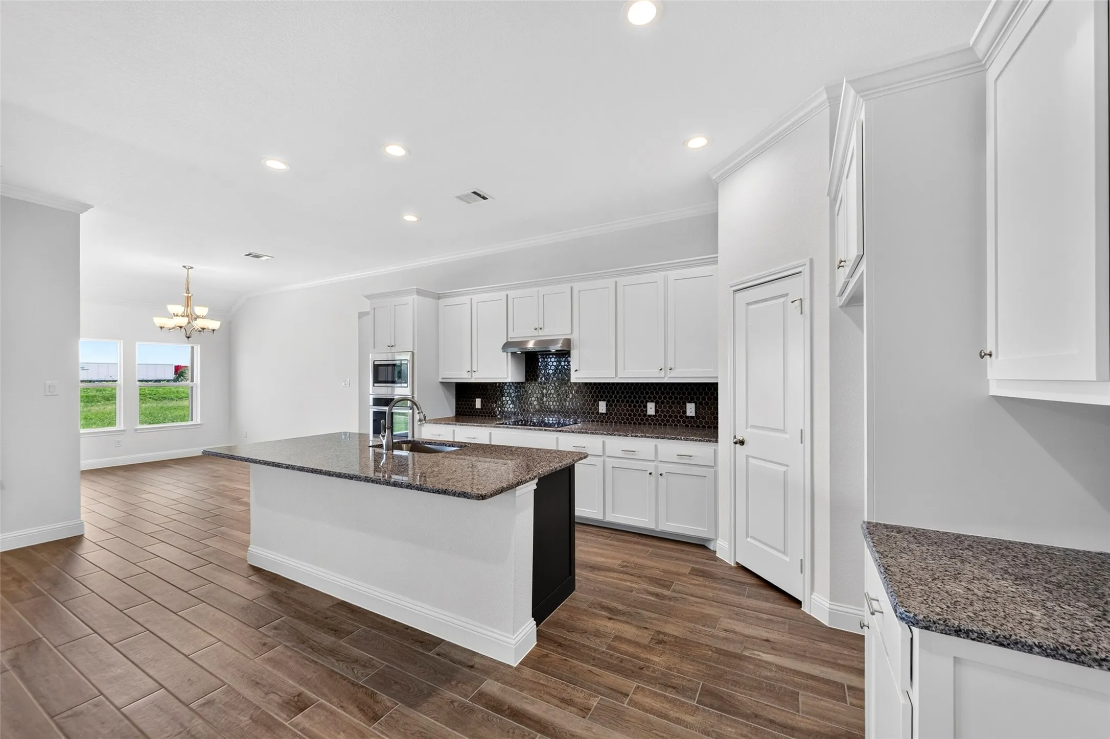 Open-concept kitchen featuring an island with a sink, white cabinetry, dark granite-finish countertops, wood-finish flooring, and recessed lighting
