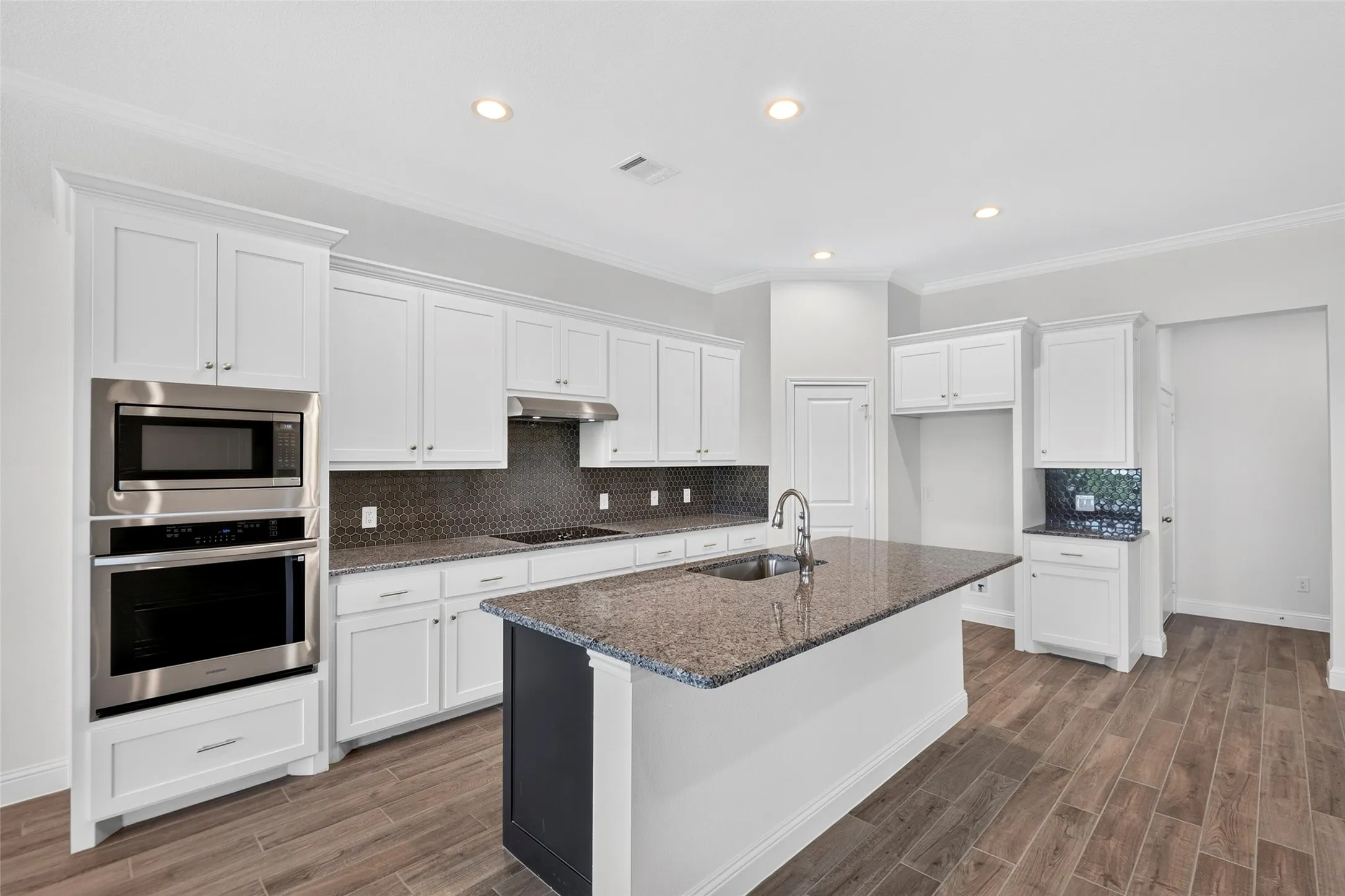 Spacious kitchen featuring an expansive center island with an undermount sink, white cabinetry, dark stone countertops, a tiled backsplash, and wood-finish flooring