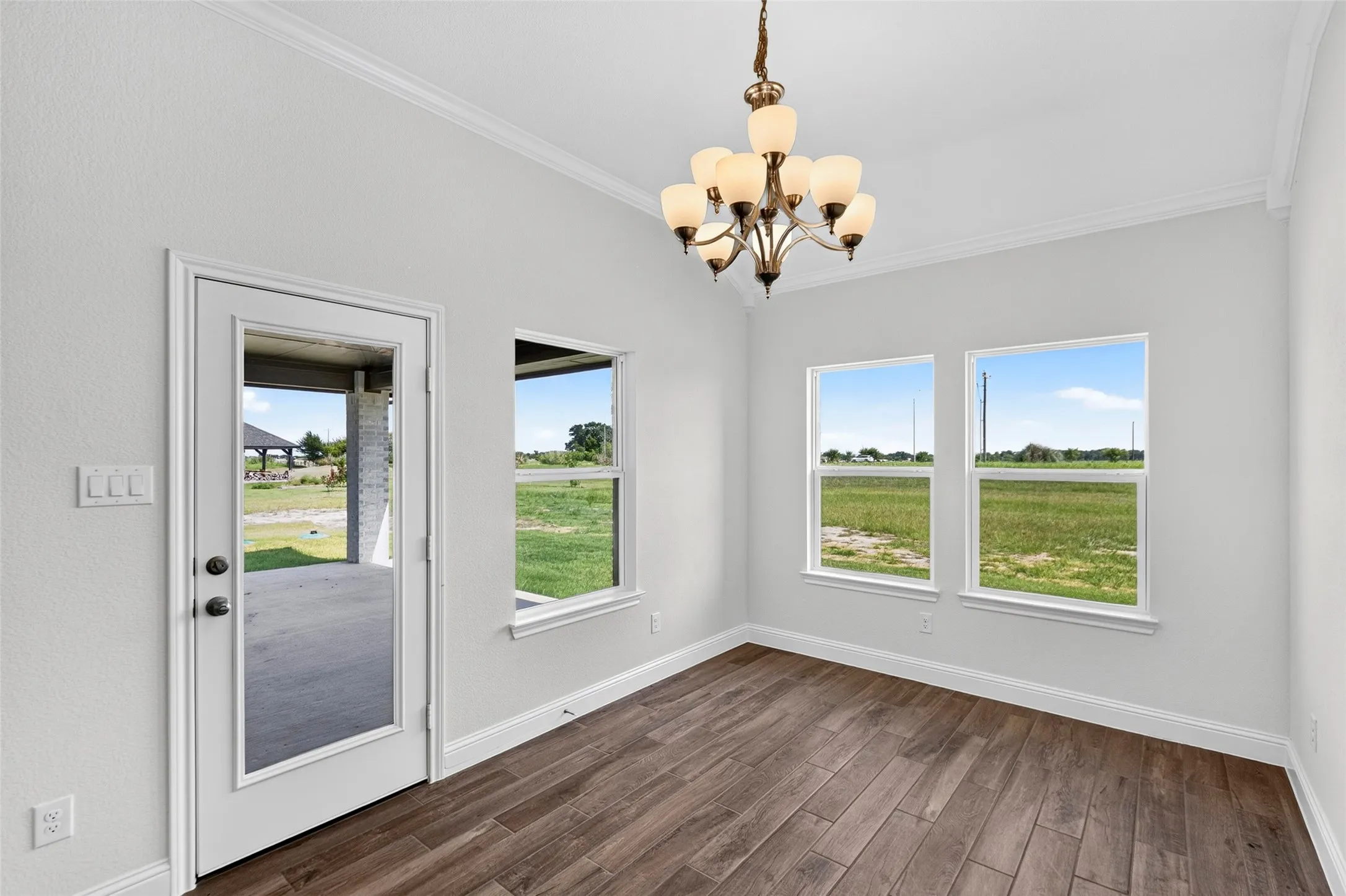 Interior space with wood-finish flooring, two large windows, and a glass-paneled exterior door leading to a covered patio