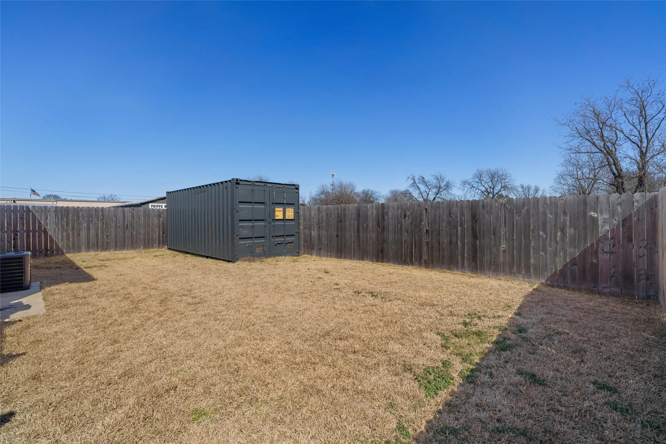 Spacious backyard featuring a dark gray storage container, wood privacy fencing, and a concrete pad