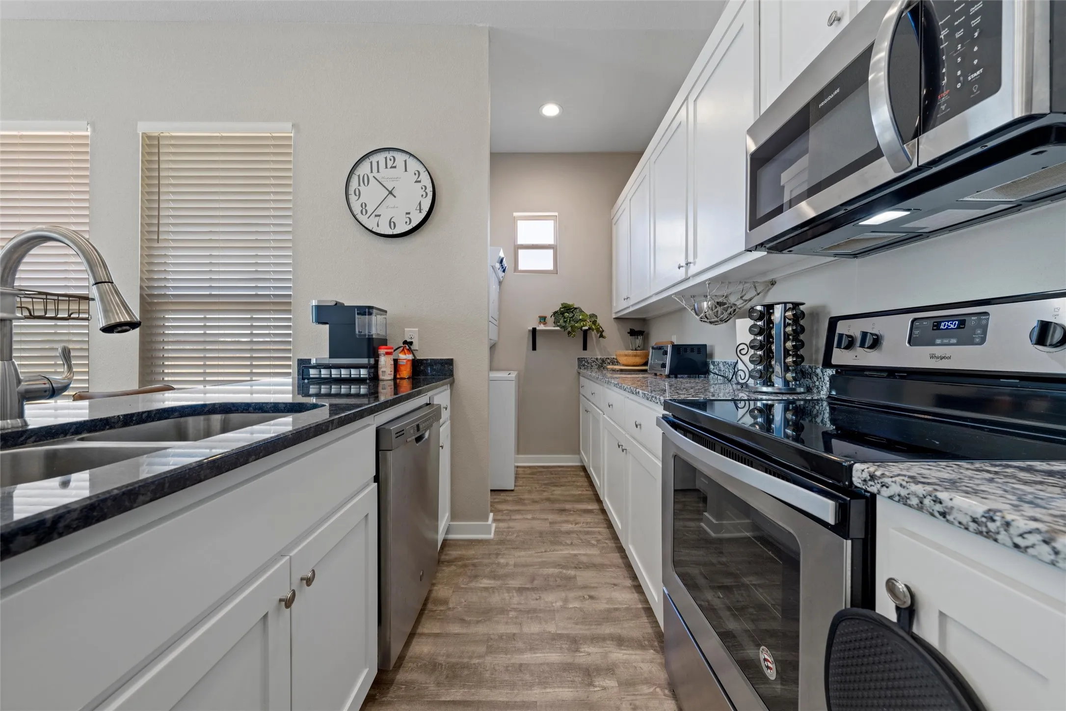 Galley kitchen featuring white cabinetry, stainless steel appliances, dark stone countertops, wood-finish flooring, and recessed lighting