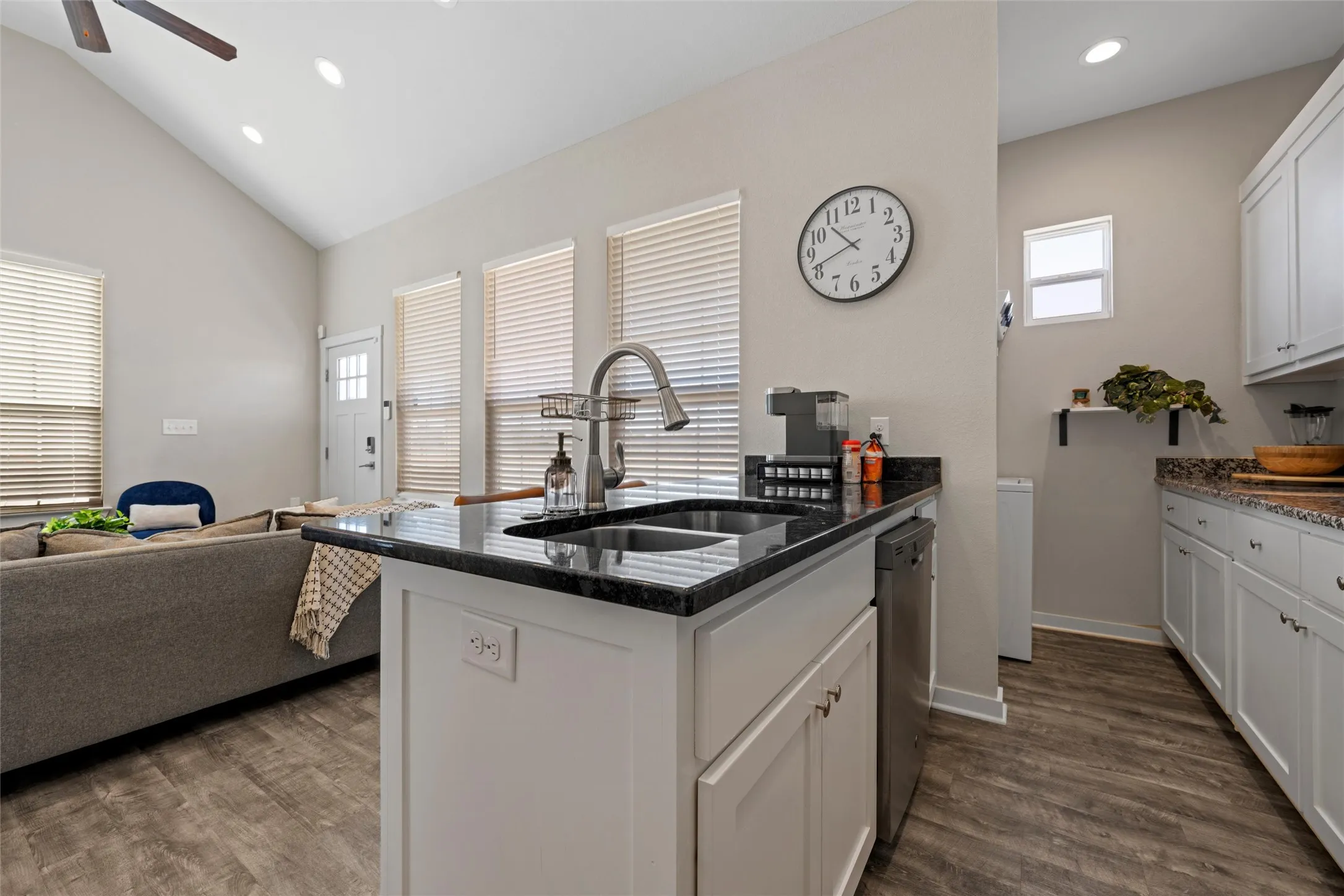 Kitchen island with an undermount sink and gooseneck faucet, black countertop, white shaker cabinetry, and stainless steel dishwasher