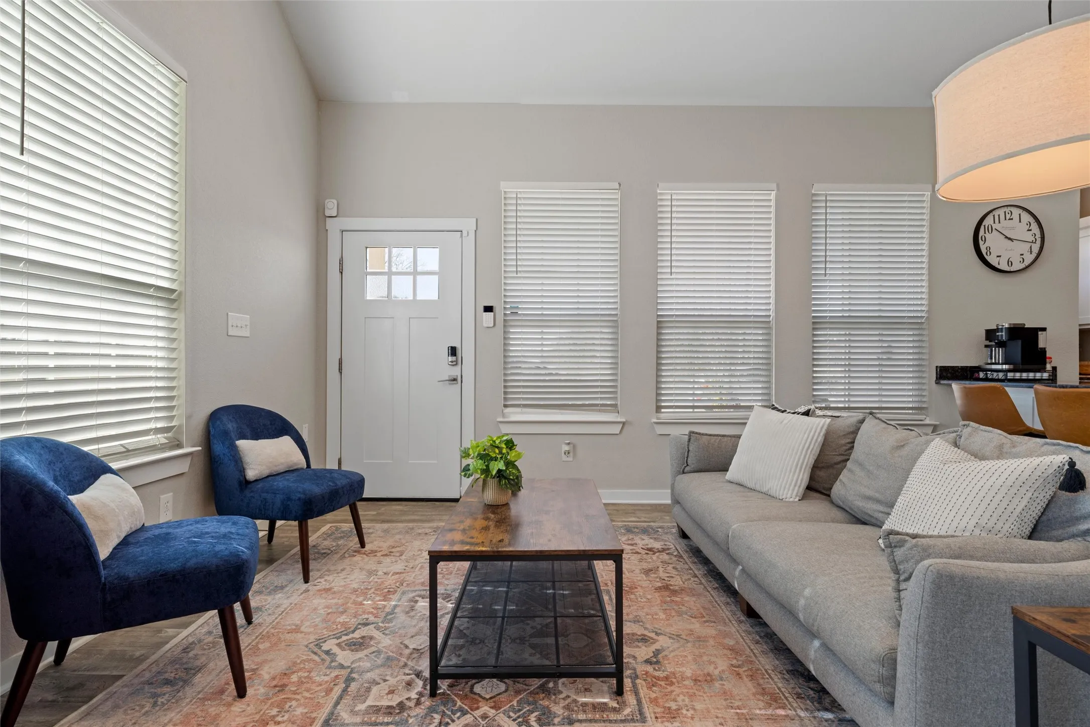 Living area featuring light-toned walls, wood-finish flooring, and multiple windows with blinds