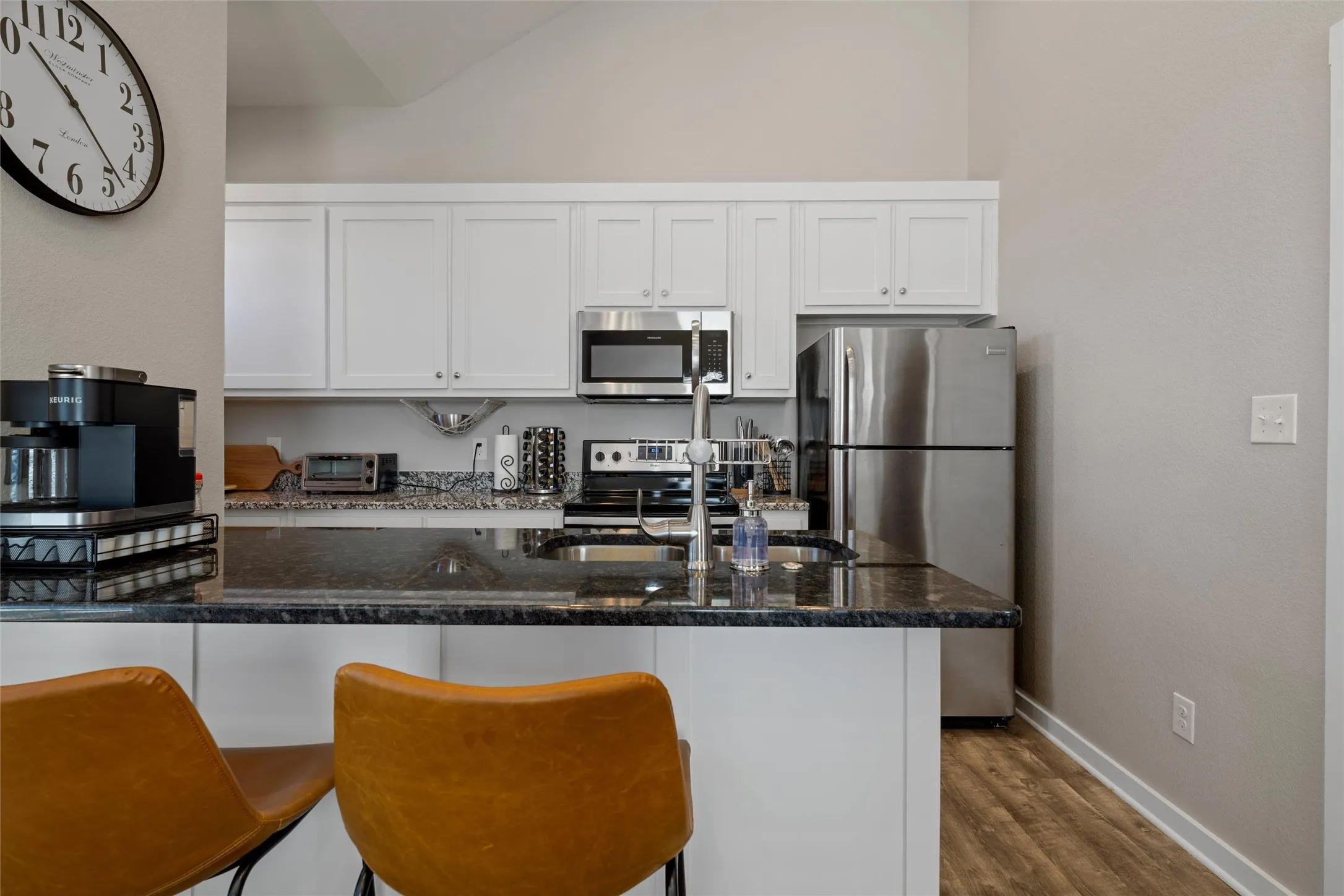 Kitchen featuring white cabinetry, stainless steel appliances, dark stone countertops, and wood-finish flooring