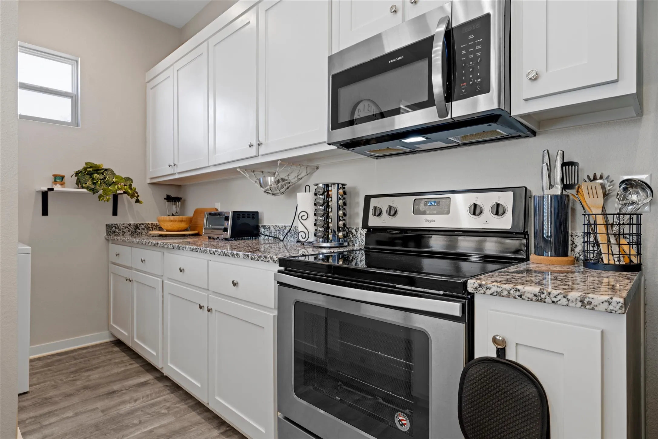 Kitchen featuring white cabinetry, stainless steel appliances, granite countertops, wood-finish flooring, and a window