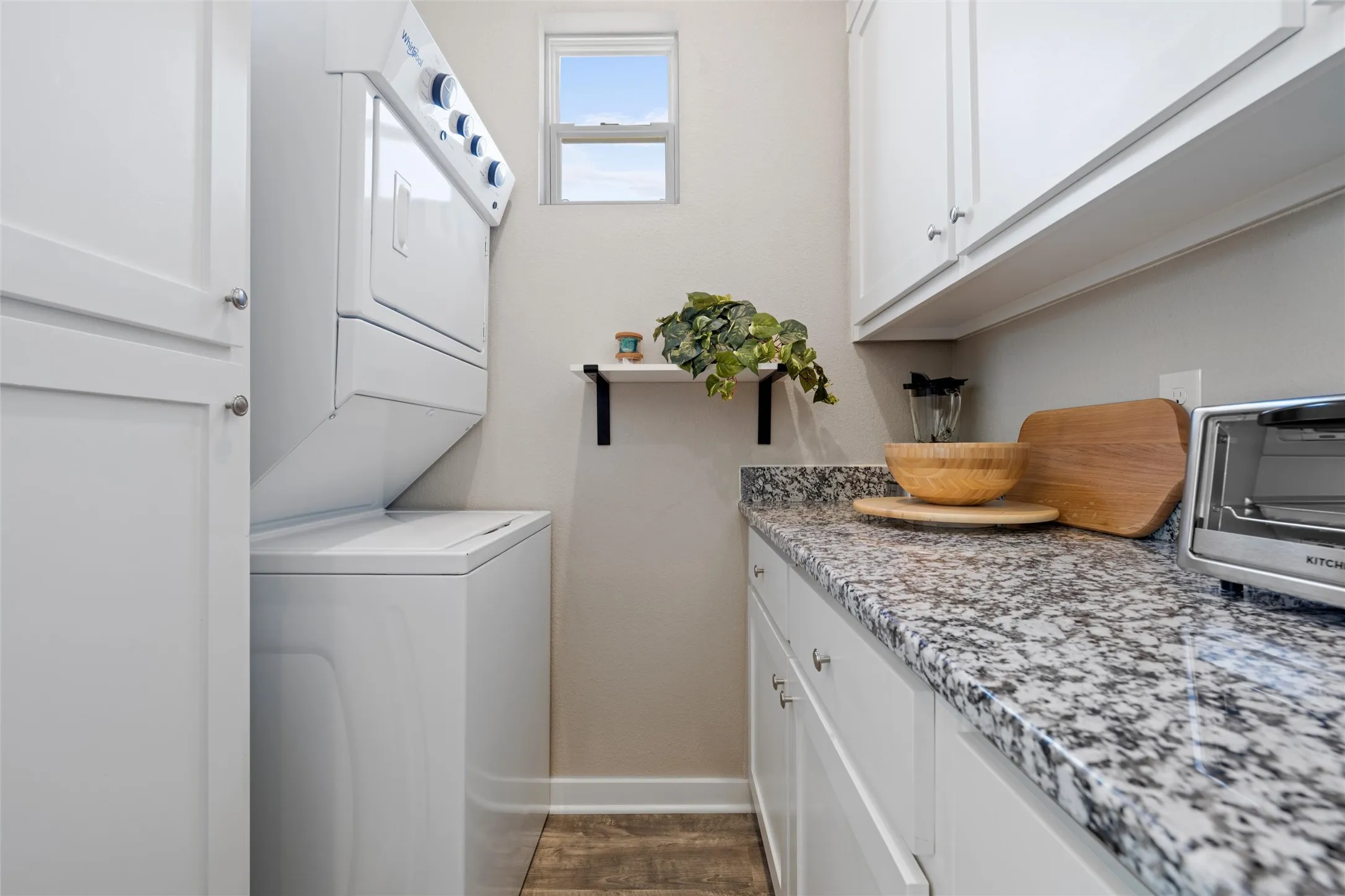 Dedicated utility space featuring stacked washer and dryer appliances, wood-finish flooring, white shaker-style cabinetry, and speckled granite-style countertops