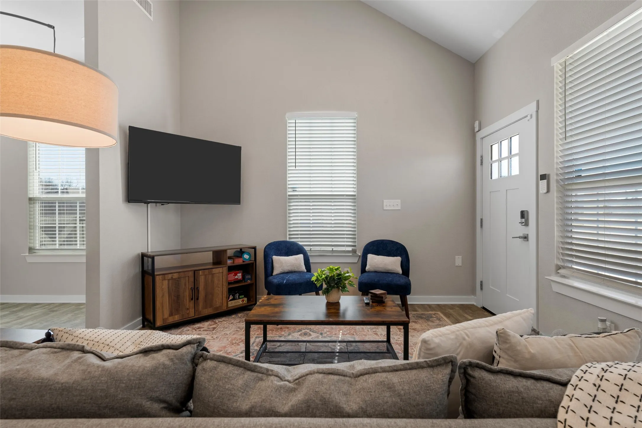 Vaulted ceiling living area featuring light neutral paint, wood-finish flooring, white trim, and ample natural light from multiple windows