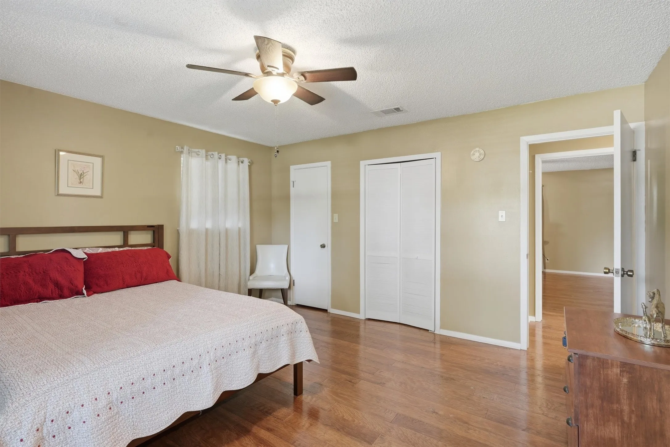 Bedroom featuring wood flooring, a ceiling fan with integrated lighting, and a window with white curtains