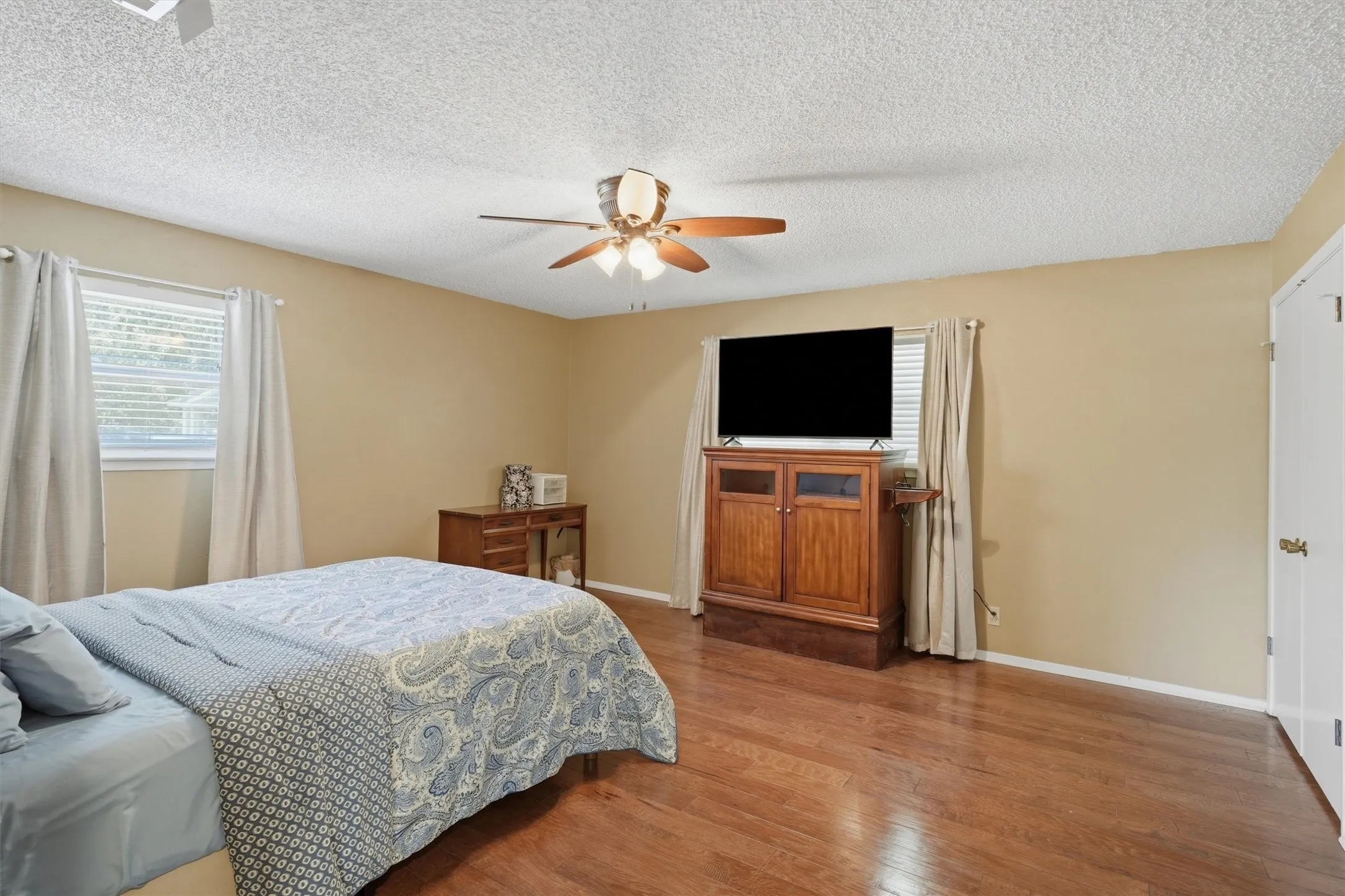 Spacious room featuring wood flooring, a ceiling fan with integrated lighting, and multiple windows with blinds