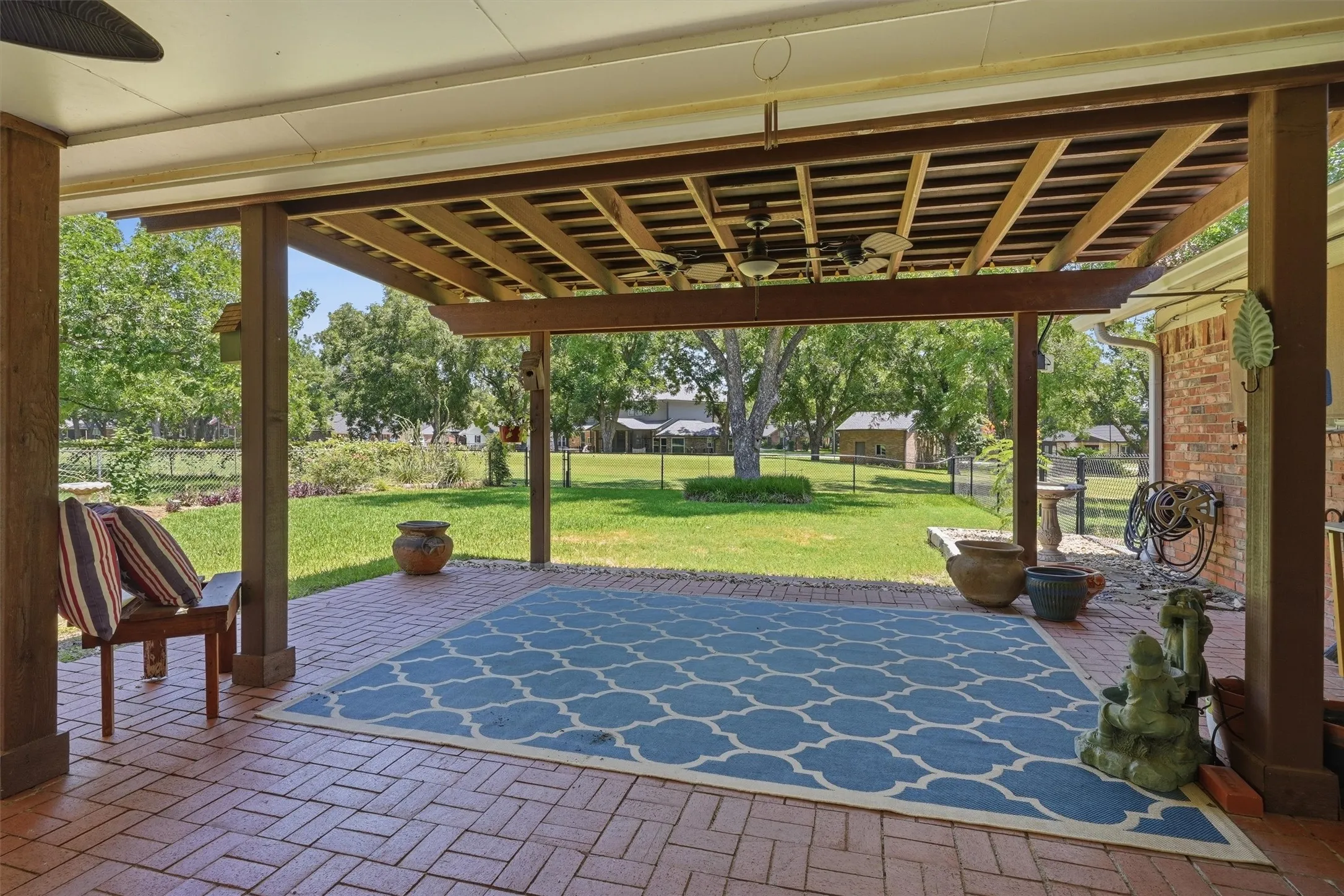 Covered patio featuring brick flooring, exposed beam ceiling, ceiling fans, and a spacious backyard with mature trees
