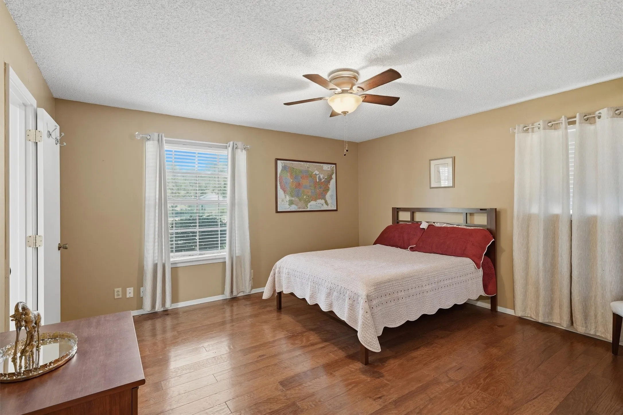 Spacious room featuring wood flooring, a ceiling fan with integrated lighting, and two windows with blinds and curtains