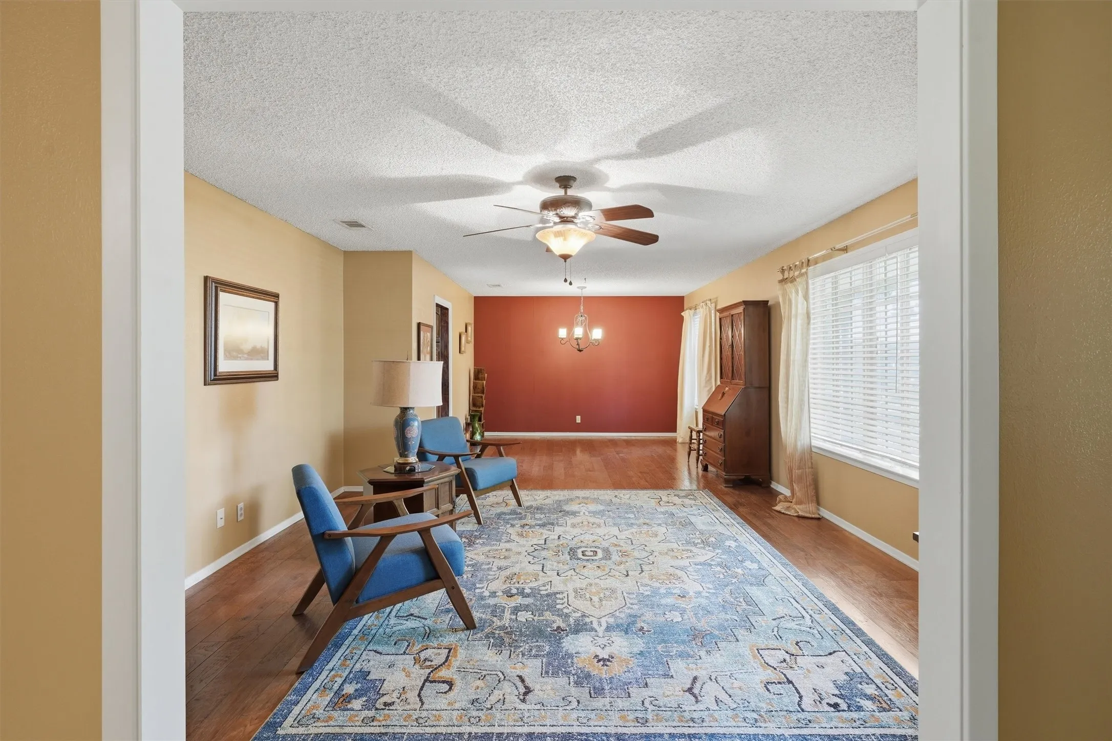 Spacious open-concept living area featuring wood-finish flooring, a ceiling fan with integrated lighting, and ample natural light from a large window with blinds