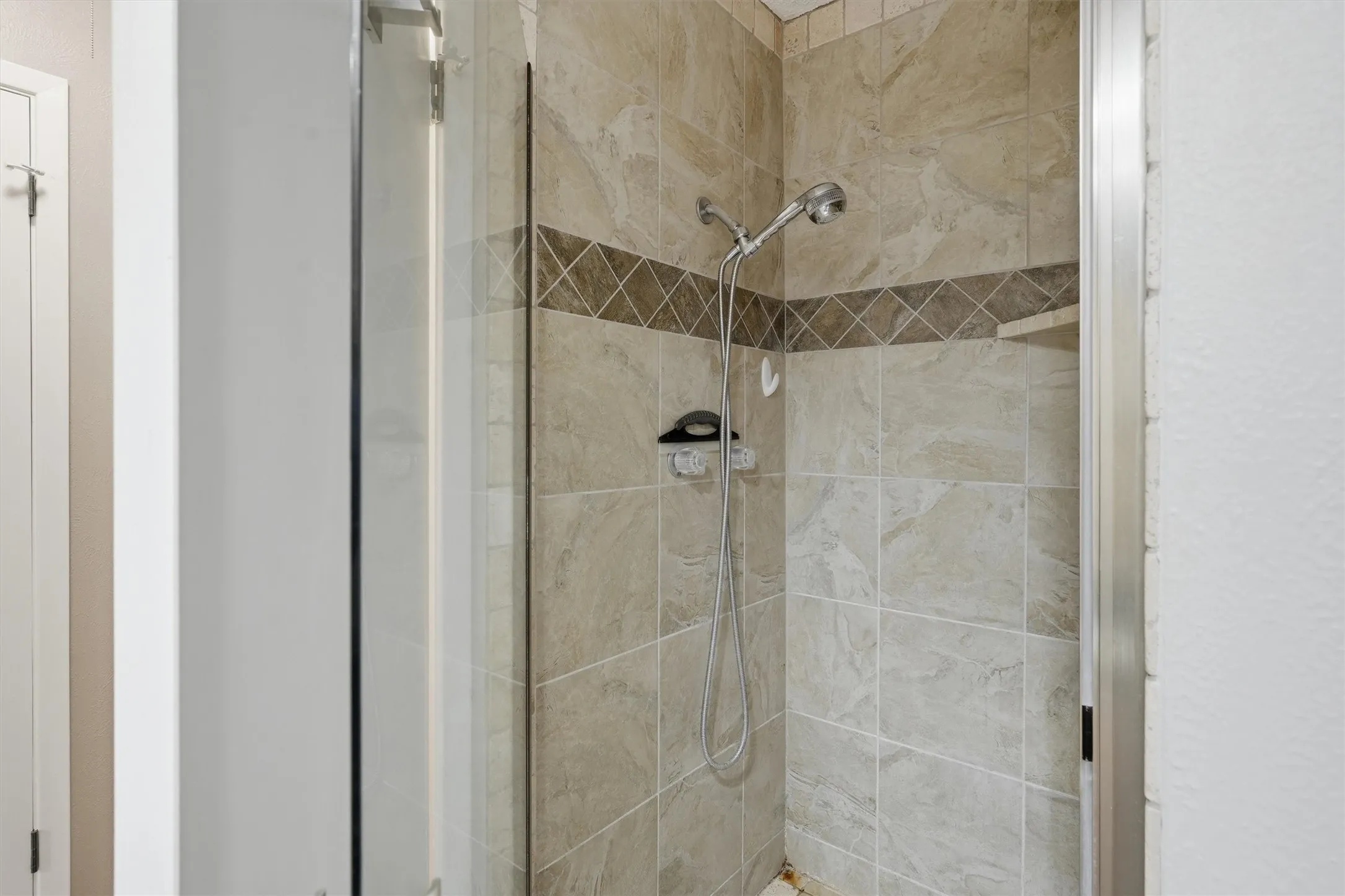 Tiled shower enclosure featuring a handheld showerhead, built-in recessed shelf, and decorative accent band