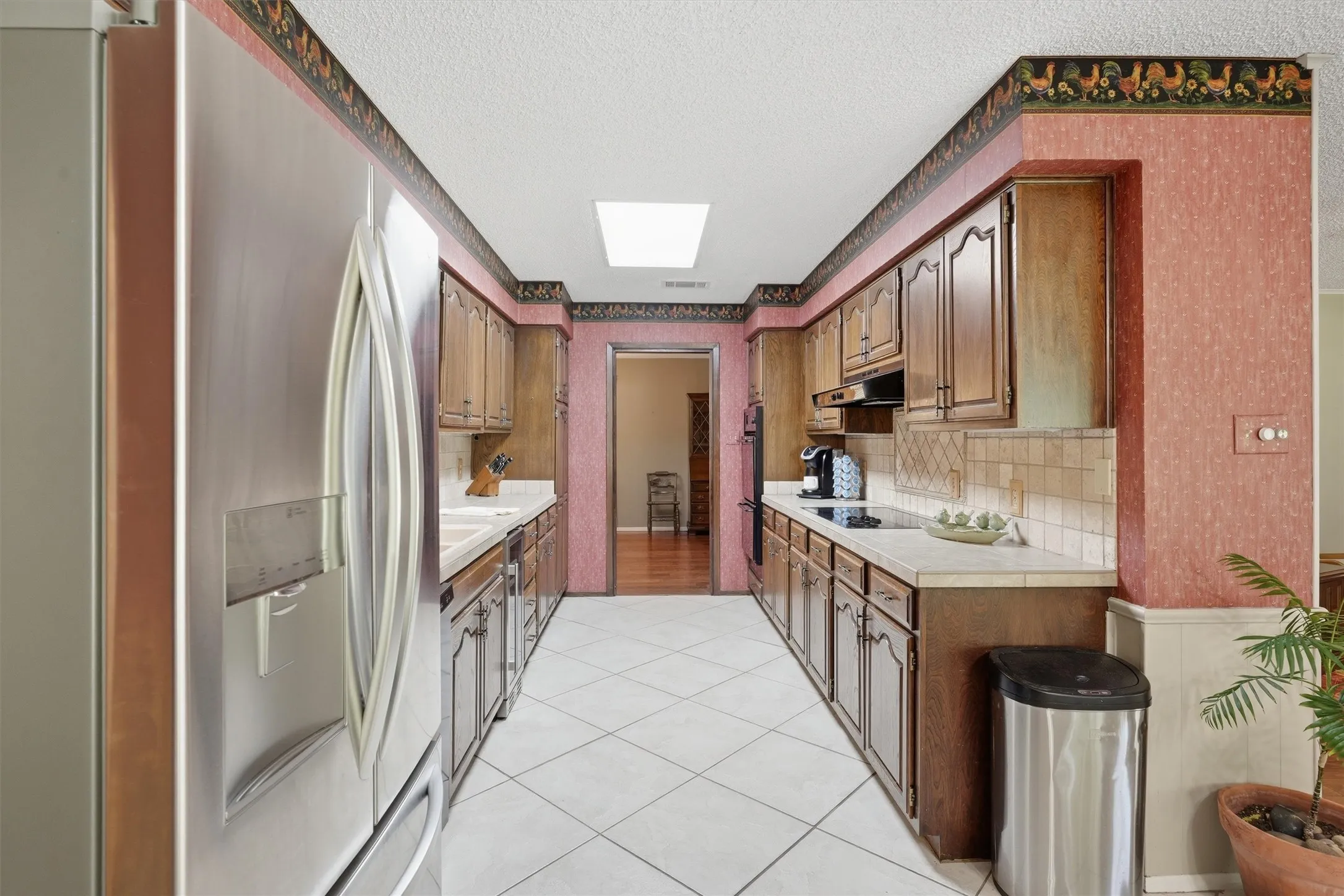 Galley kitchen featuring wood cabinetry, white tile flooring, and a skylight