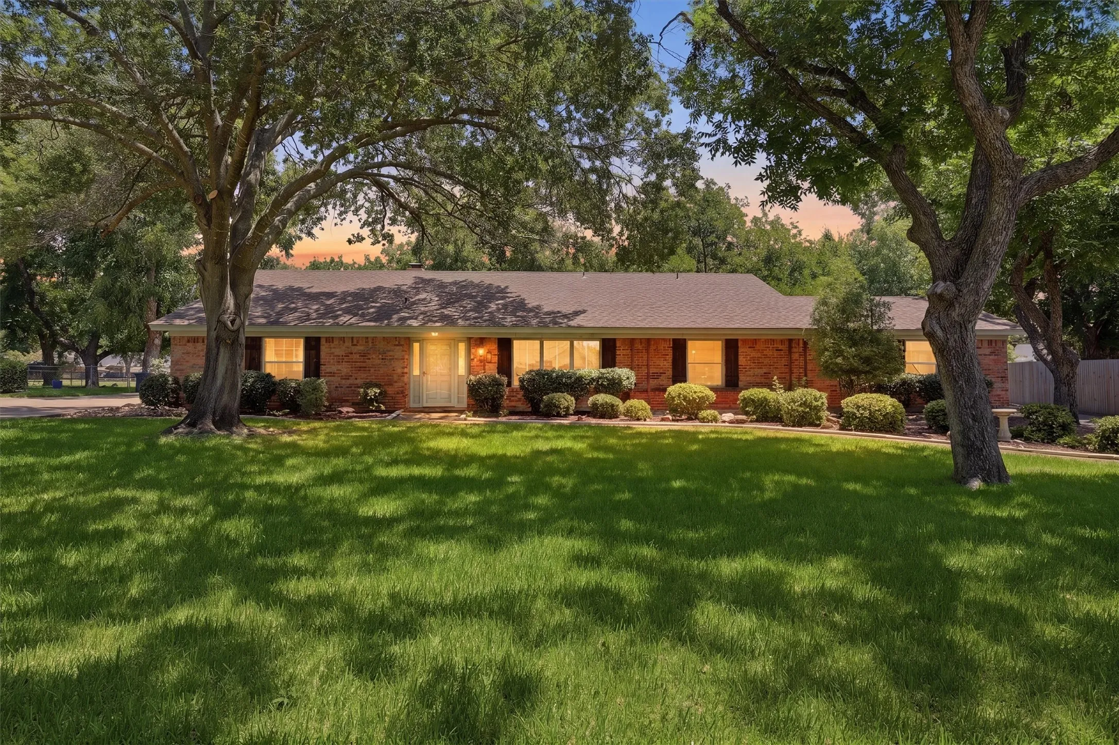 Ranch-style residence featuring a brick facade, dark roofing, and a prominent front door
