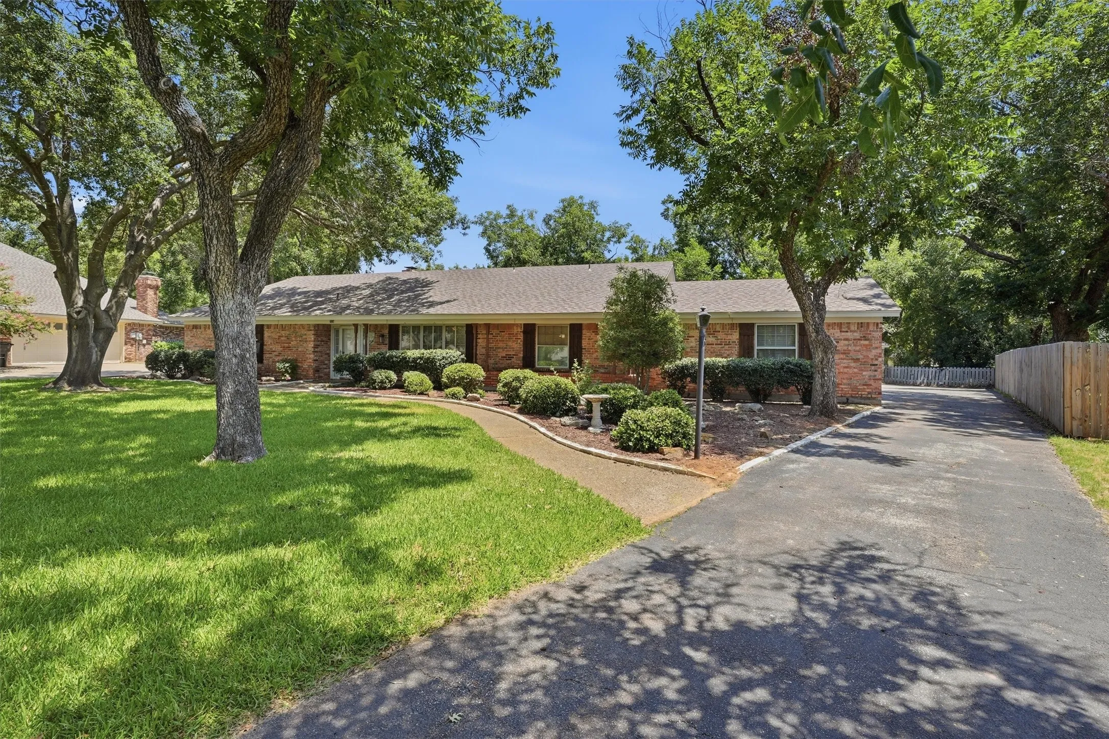 Brick ranch-style exterior featuring a prominent front lawn with mature trees
