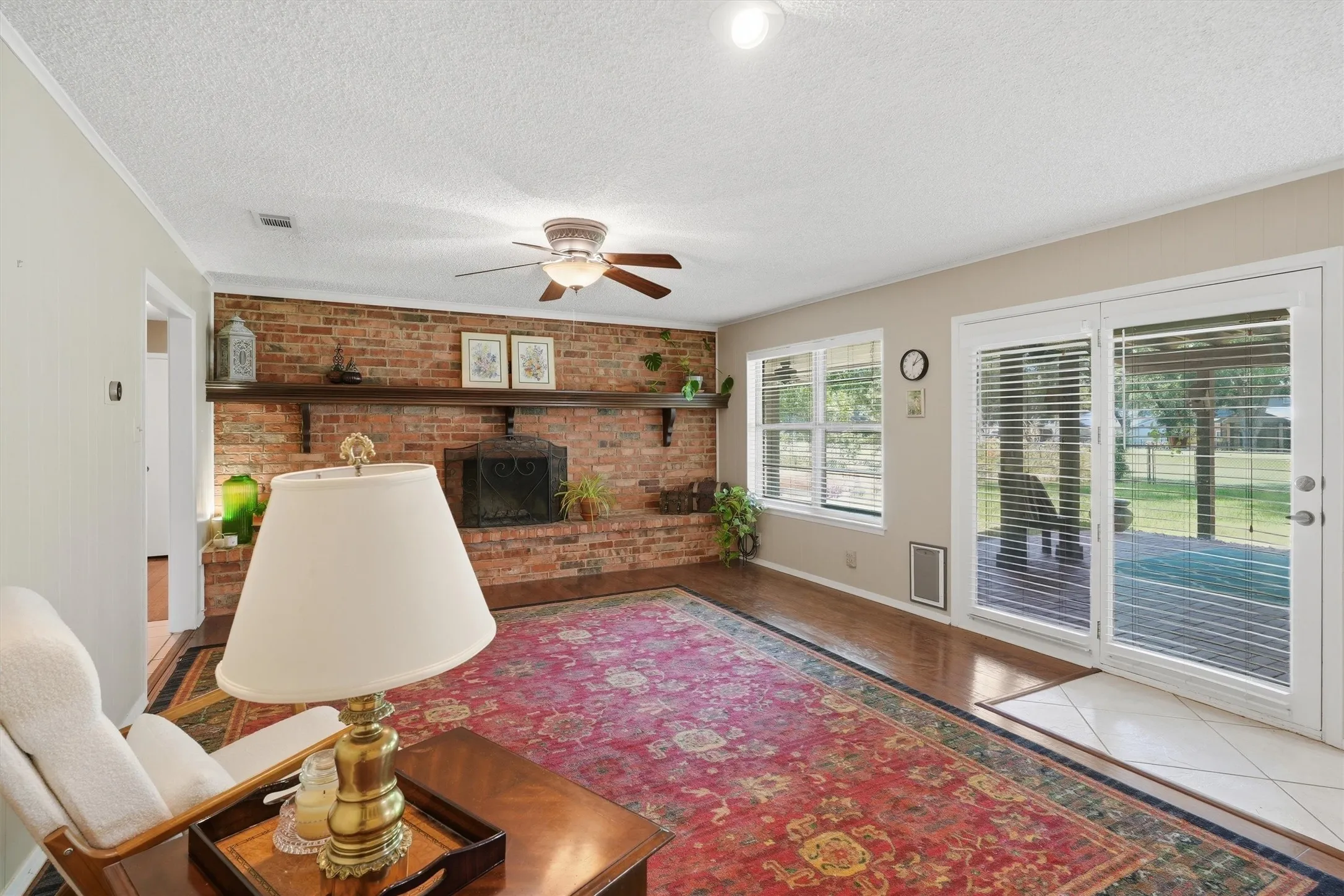 Spacious living area featuring a prominent brick fireplace with a wood mantel, wood-finish flooring, and a ceiling fan