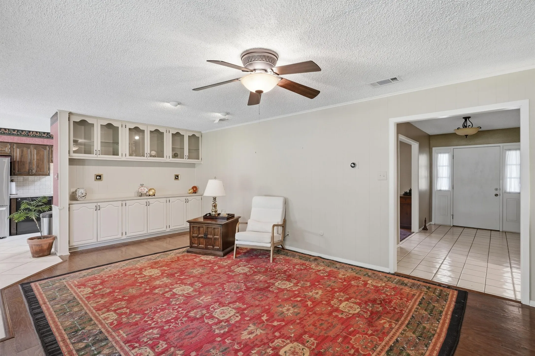 Living area featuring wood-finish flooring, a ceiling fan with integrated lighting, and built-in cabinetry with glass-front uppers