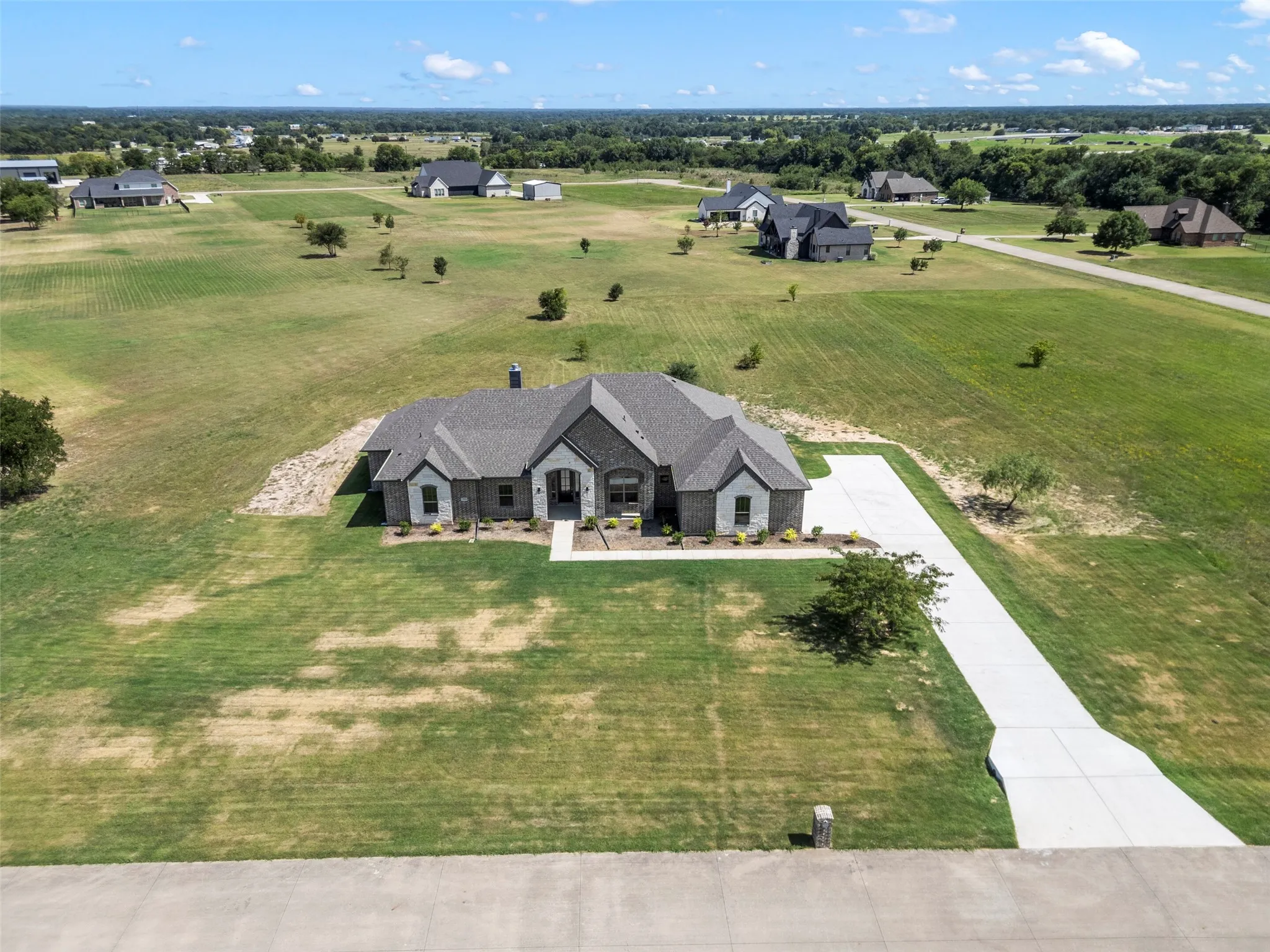 Expansive property featuring a contemporary home with a dark brick and light stone exterior, a concrete driveway, and a large manicured lawn