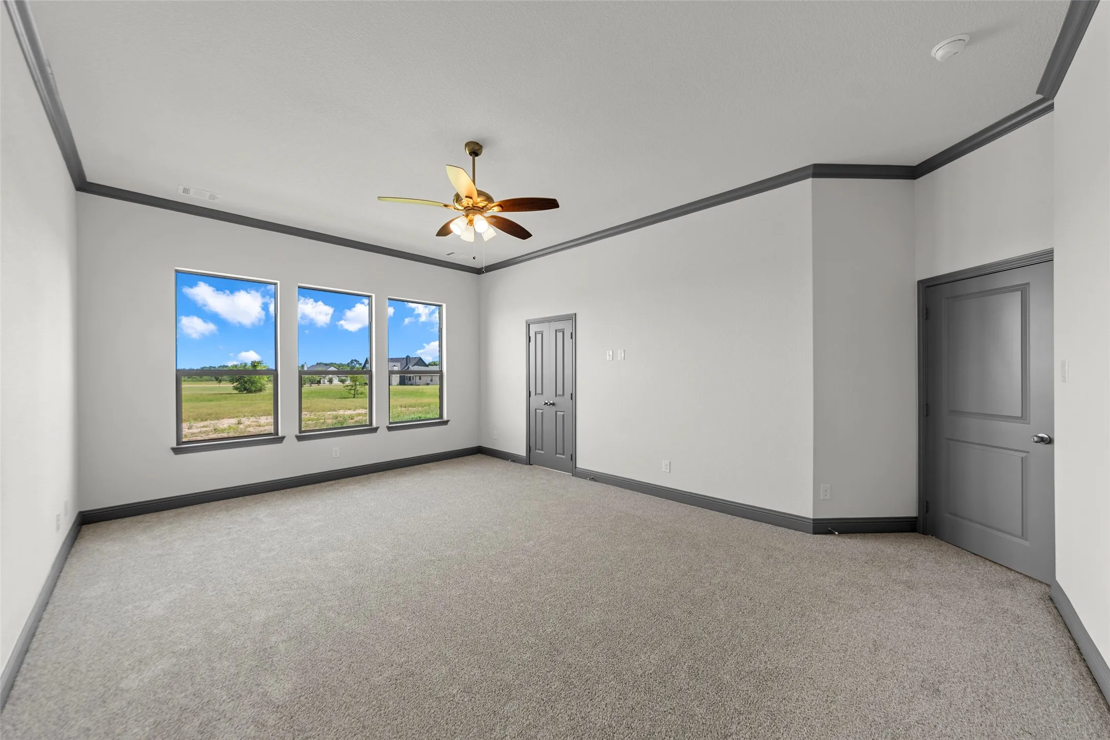 Spacious room featuring broadloom carpeting, a multi-pane window array, and an overhead ceiling fan with integrated lighting