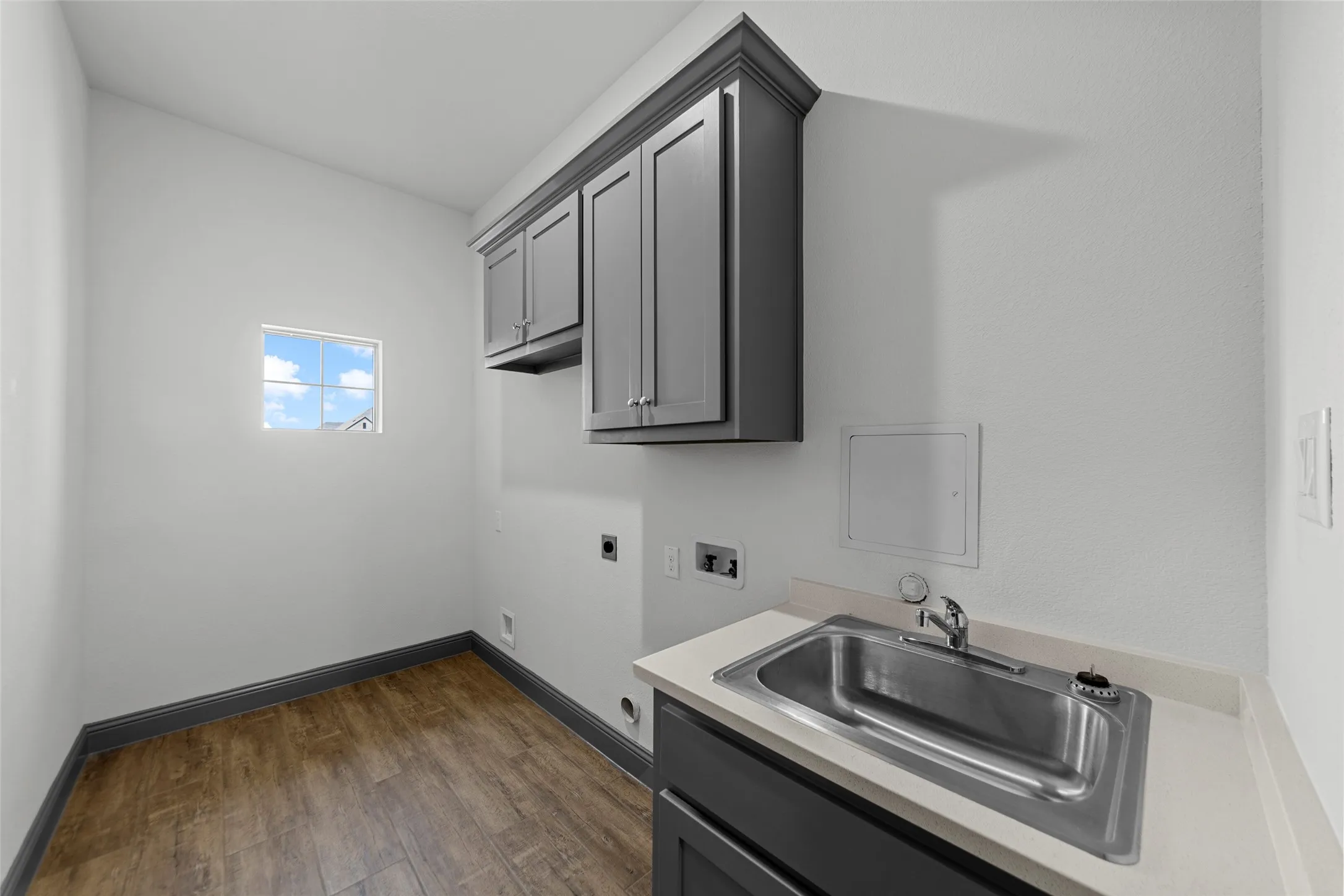 Utility room featuring wood-finish flooring, a wall-mounted window, and built-in cabinetry with a countertop and stainless steel sink