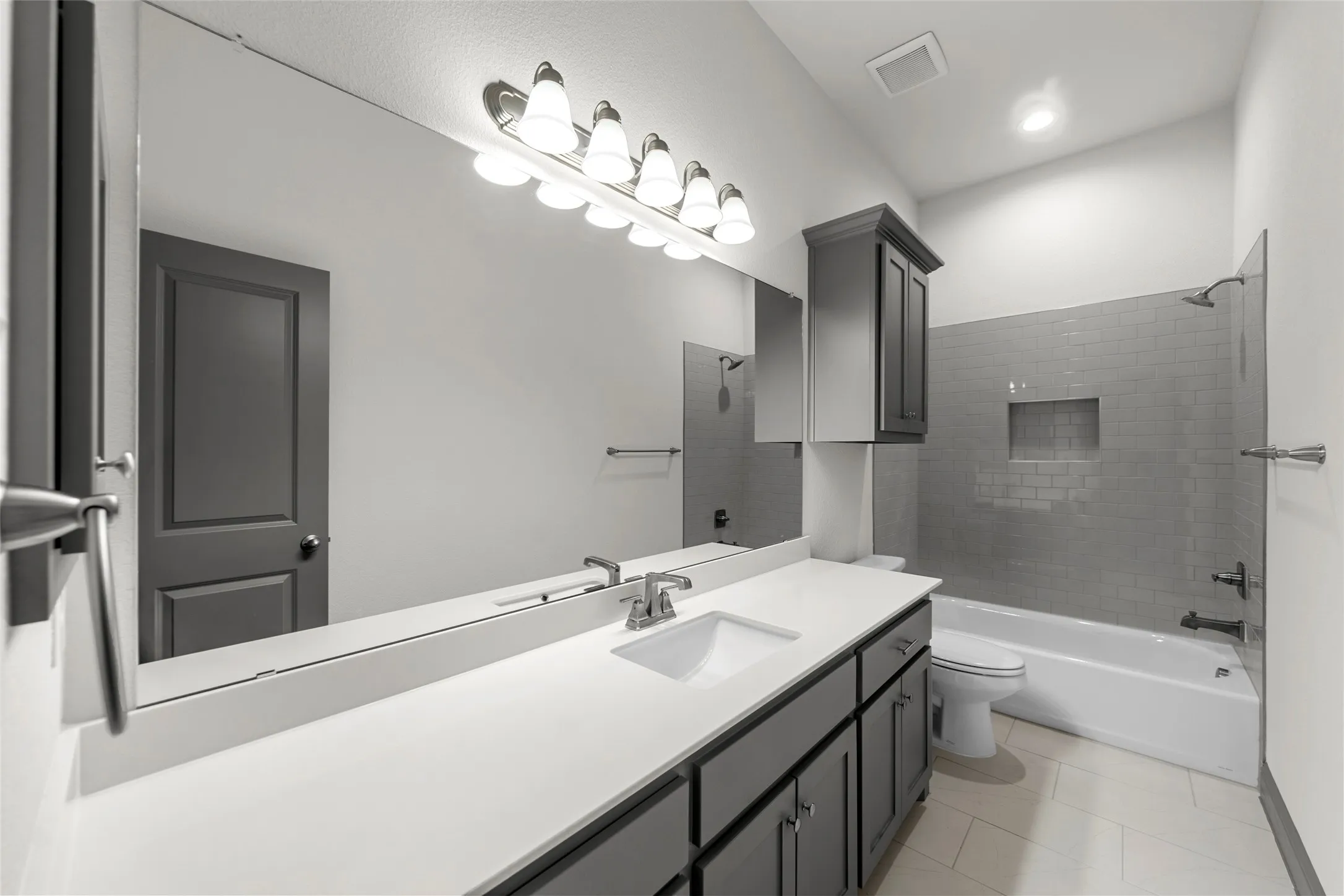 Bathroom featuring a large vanity mirror, an undermount sink, ample counter space, dark wood-finish cabinetry, and a subway tile shower surround with an integrated niche