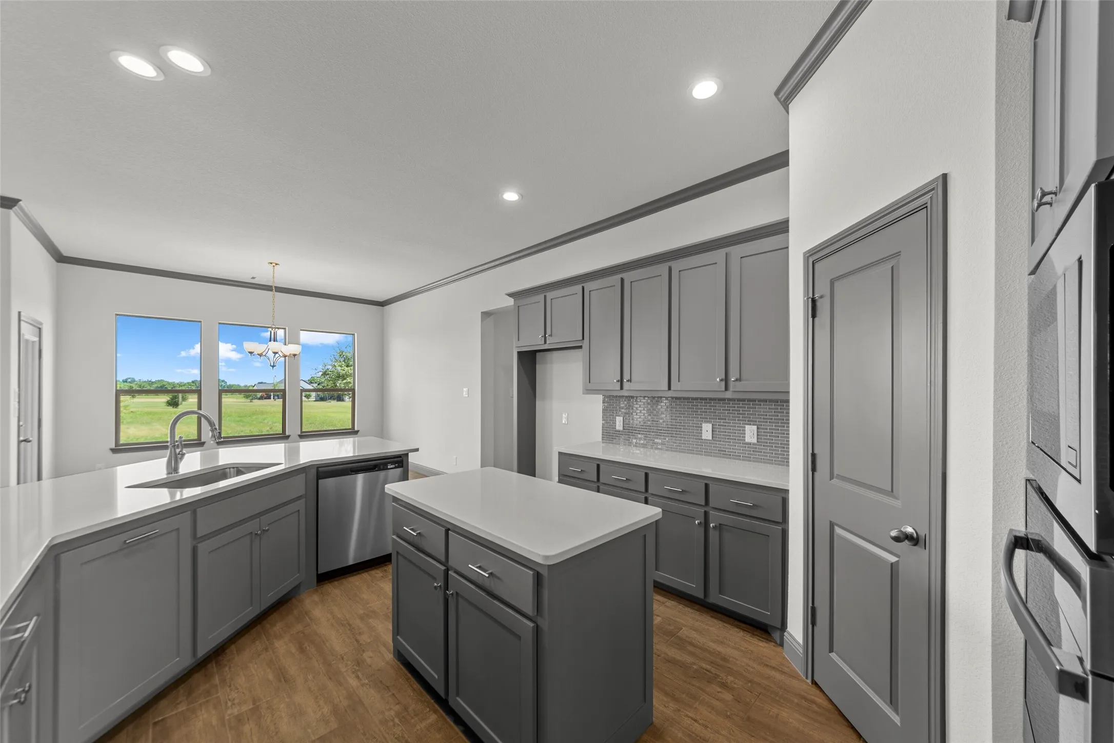Modern kitchen featuring grey cabinetry, white countertops, stainless steel appliances, and wood-finish flooring