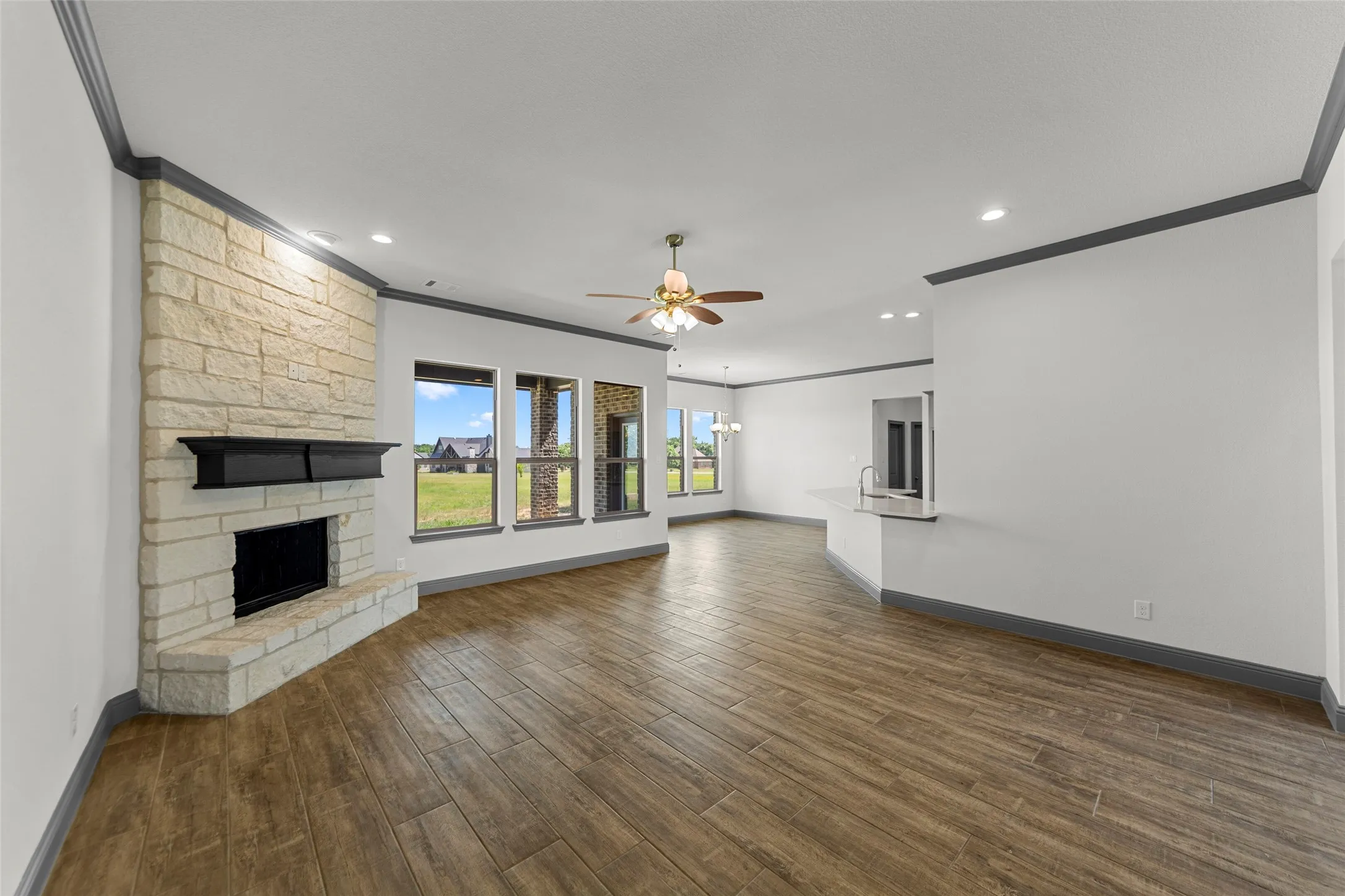 Spacious interior featuring a stone-clad fireplace with a dark mantel, wood-finish flooring, recessed lighting, and multiple windows