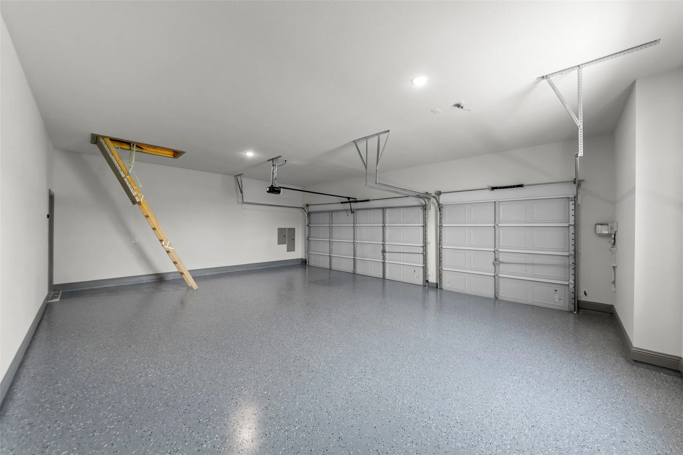 Two-car garage featuring a speckled epoxy floor coating, white walls, and a pull-down attic access ladder
