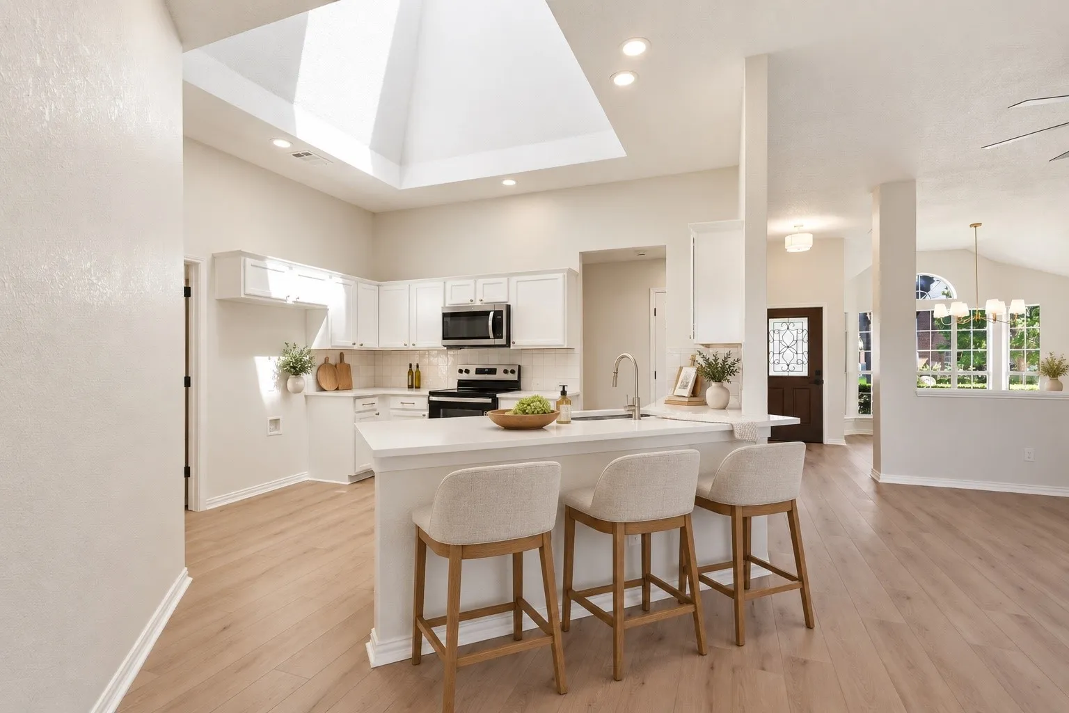 Kitchen featuring white cabinetry, stainless steel appliances, a center island with seating, wood-finish flooring, and a skylight