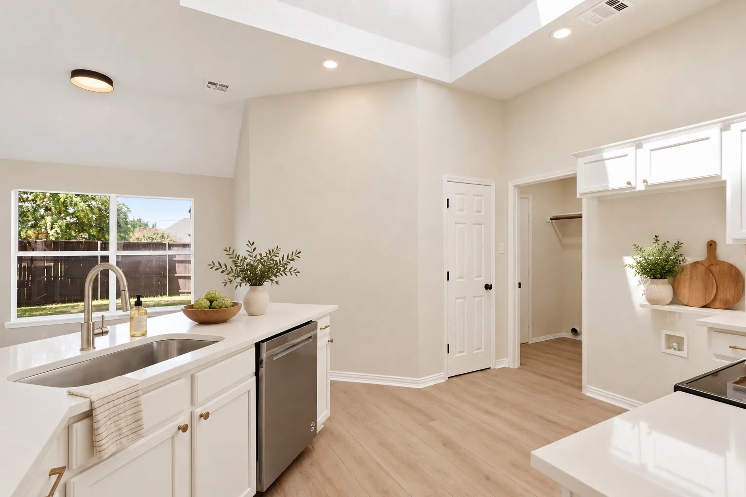 Vaulted ceilings, skylight, white cabinetry, integrated stainless steel dishwasher, and wood-finish flooring