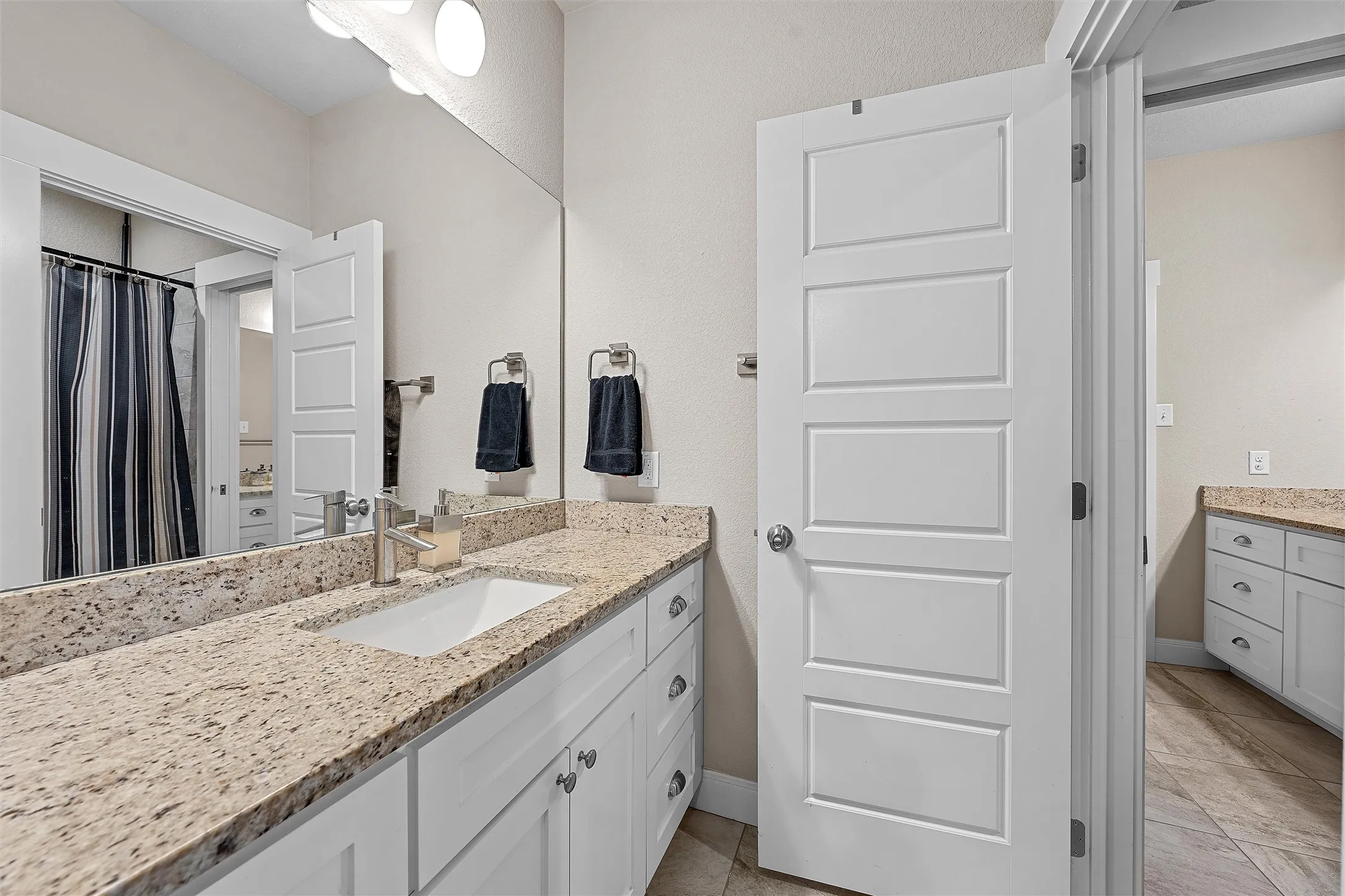 Spacious bathroom featuring a dual vanity with light-colored speckled countertops and white cabinetry