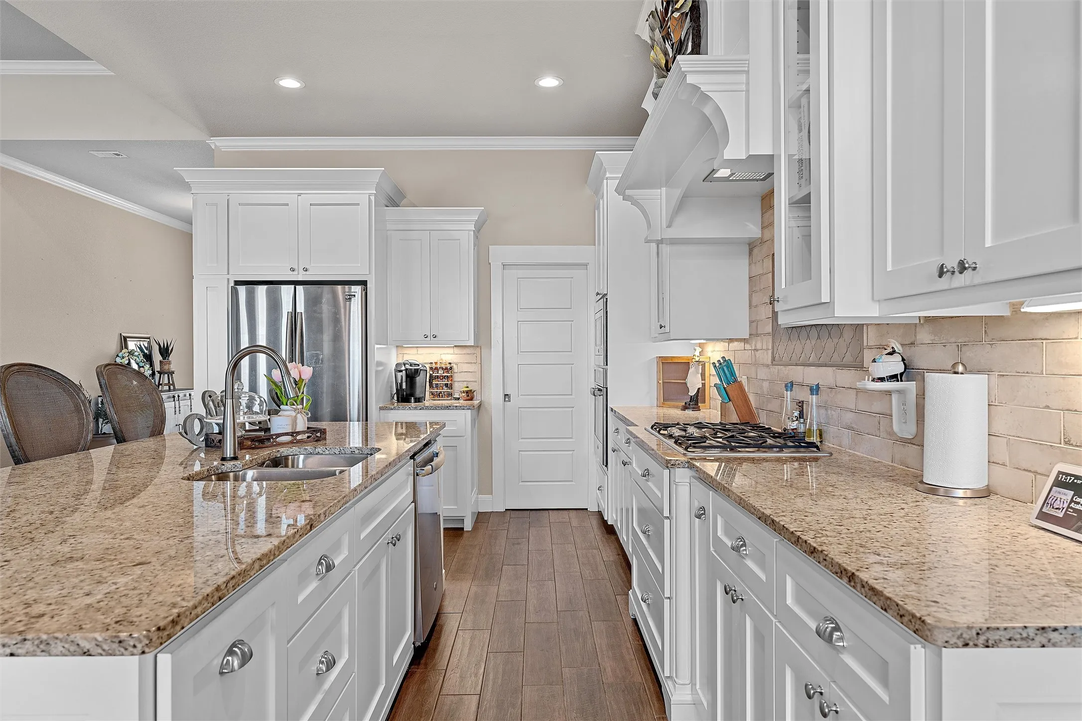 Modern kitchen featuring white cabinetry, granite countertops, wood-finish flooring, a stainless steel refrigerator, and a gas cooktop with a decorative range hood