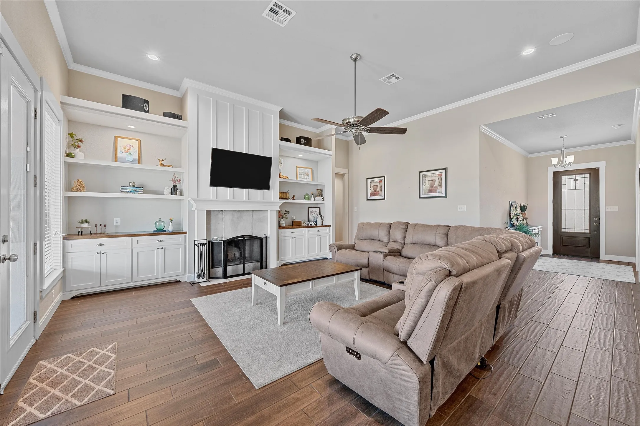 Spacious living area featuring wood-finish flooring, a ceiling fan, and built-in shelving with lower cabinetry