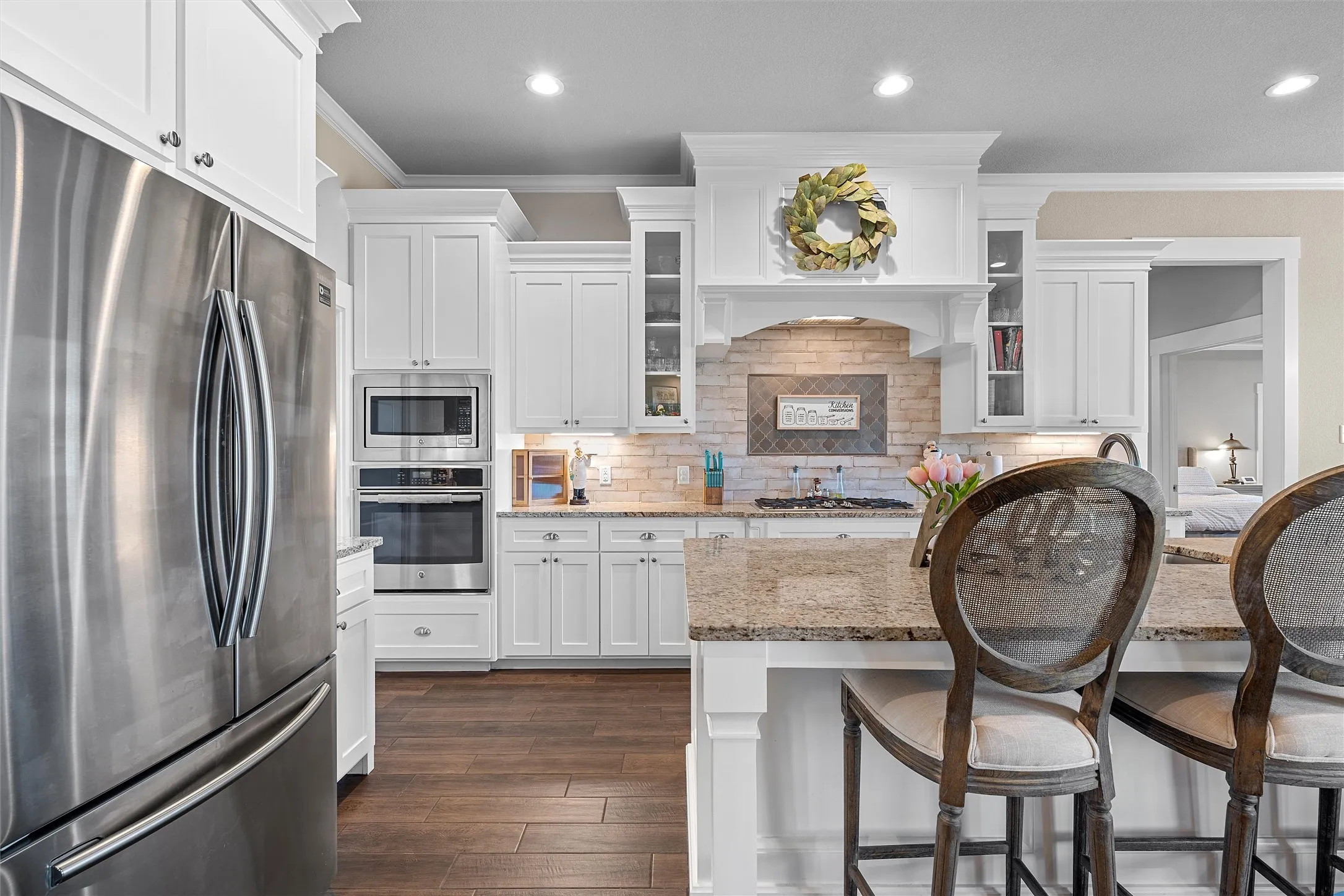 Gourmet kitchen featuring white cabinetry, built-in stainless steel appliances, granite countertops, and wood-finish flooring