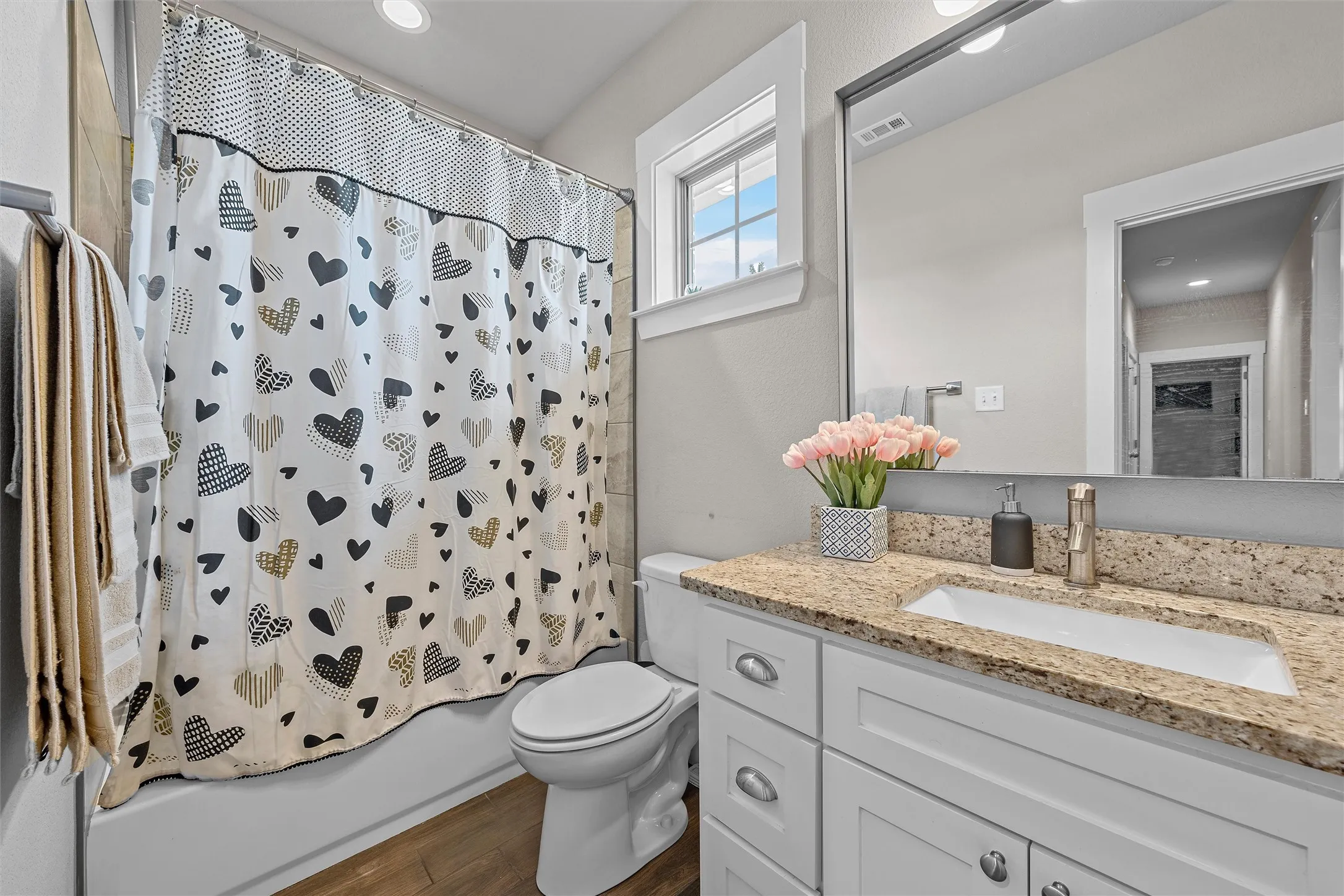 Bathroom featuring a built-in tub with a tile surround, a white toilet, and wood-finish flooring