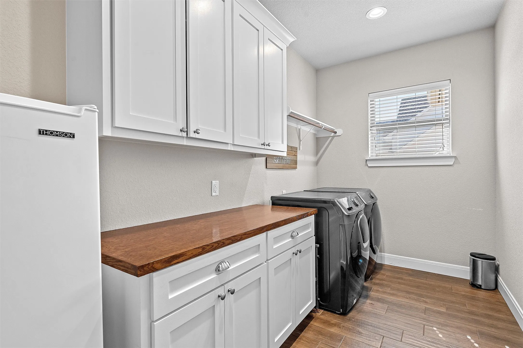 Dedicated laundry space featuring wood-finish flooring and a window with blinds