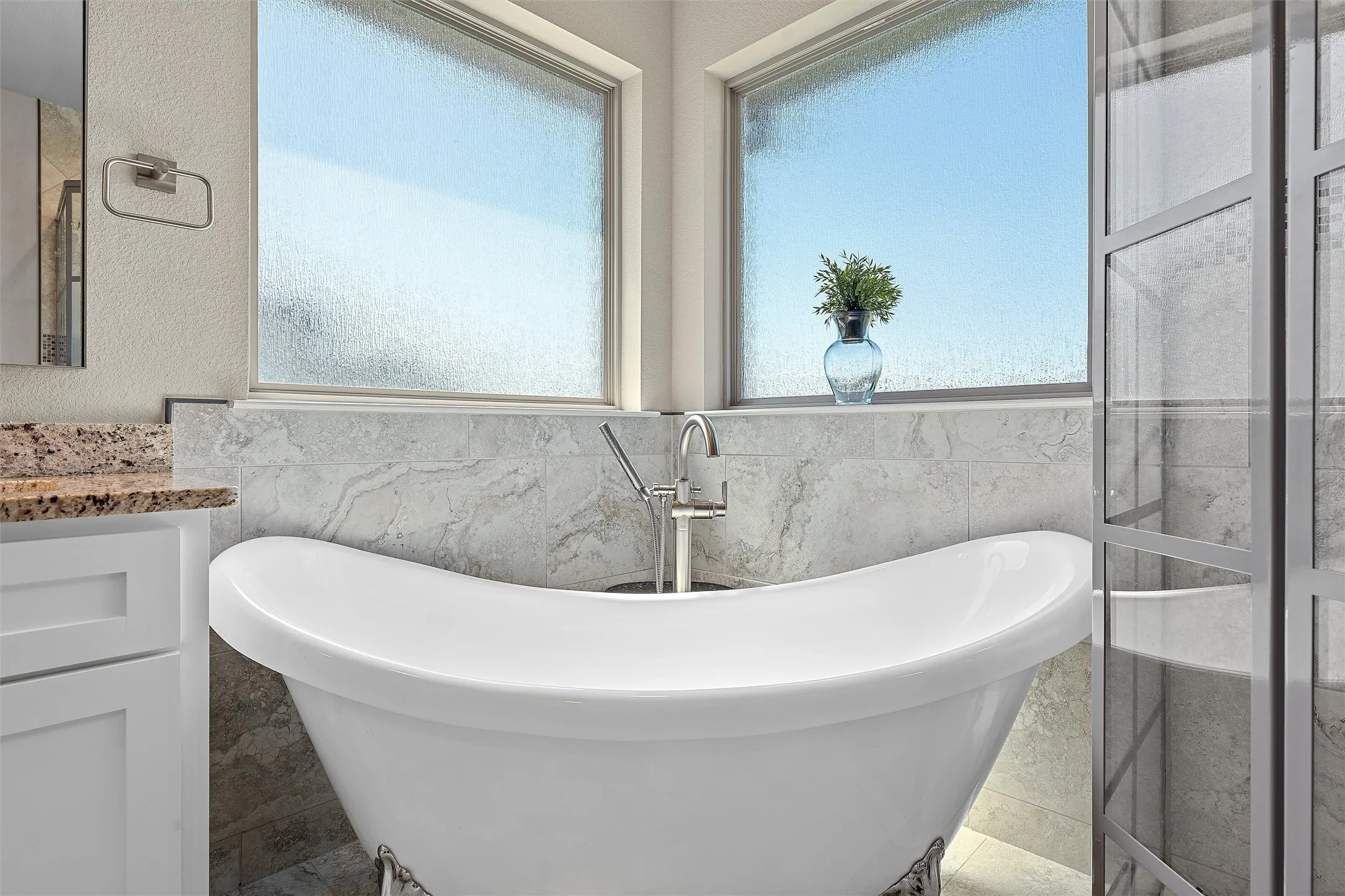 Freestanding soaking tub with a floor-mounted faucet, complemented by large format wall tile, frosted windows, and a glass-enclosed shower