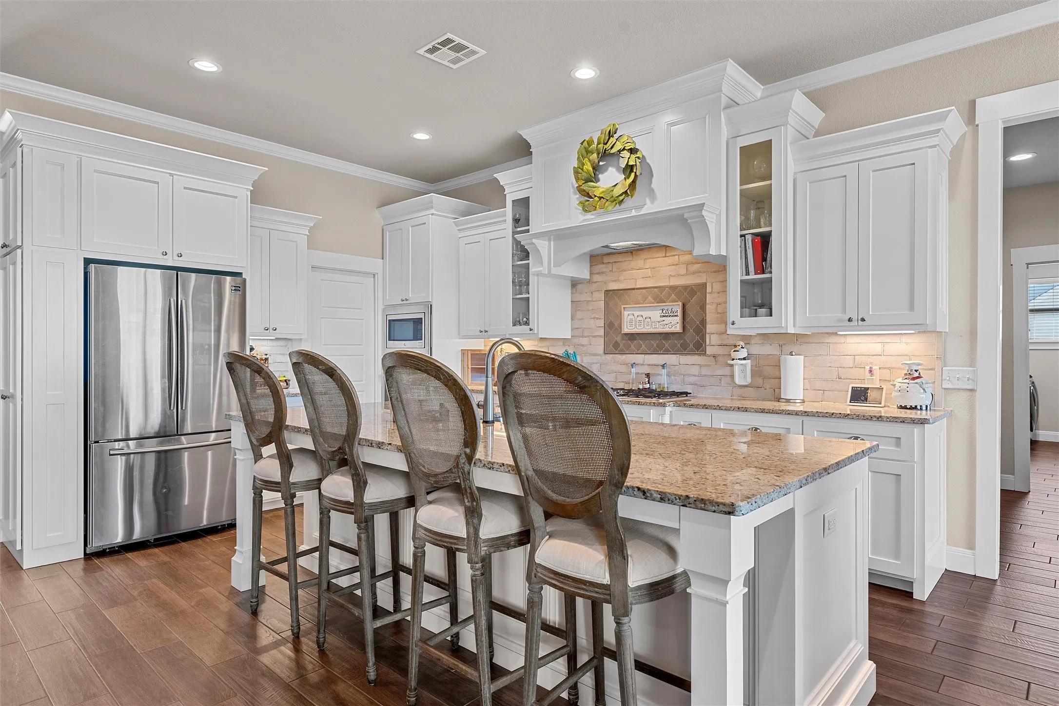 Bright kitchen featuring a central island with a stone countertop, white cabinetry with crown molding, stainless steel refrigerator, and wood-finish flooring