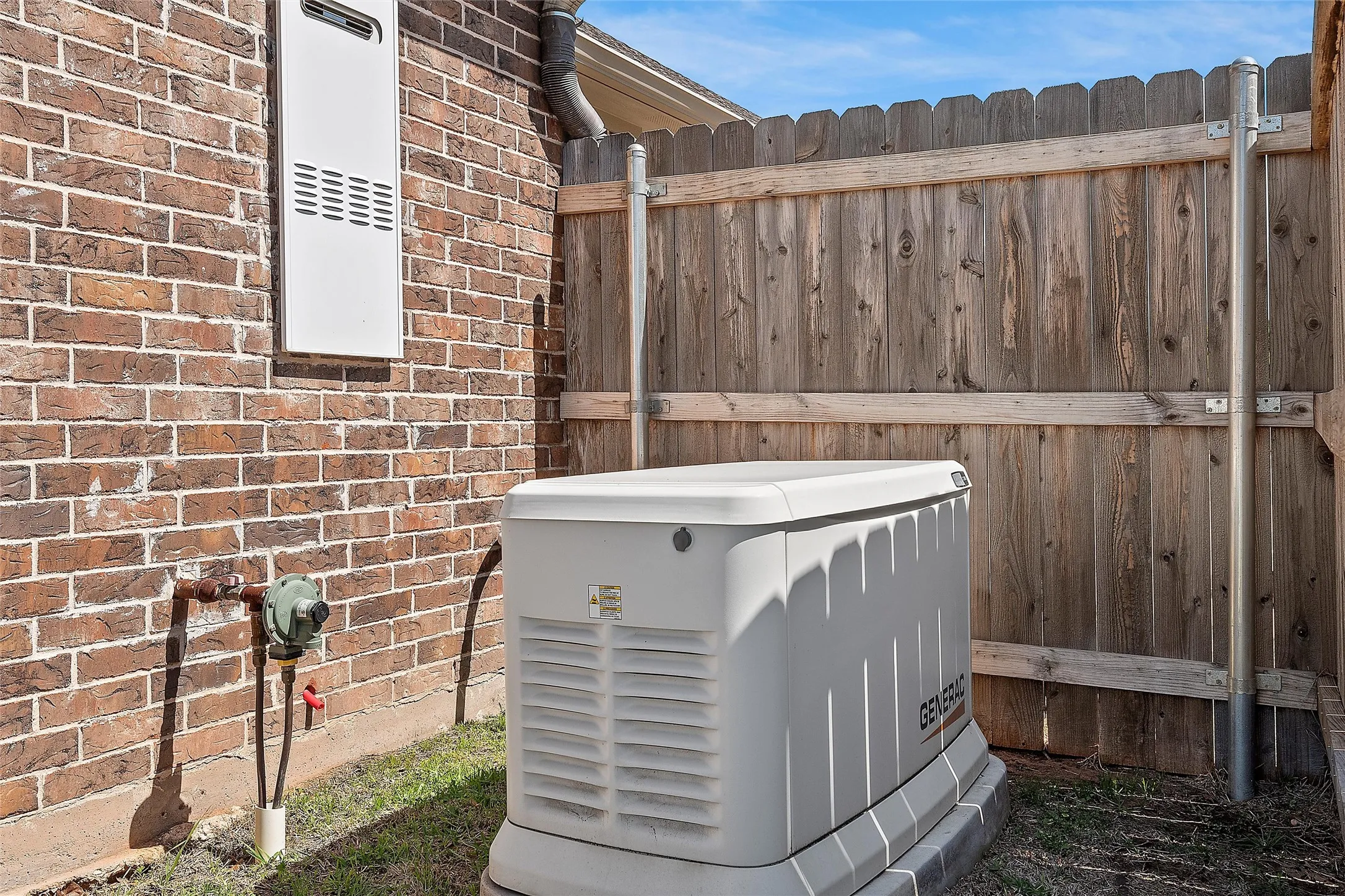 Whole-home generator system and tankless water heater, set against a brick exterior and wood fence