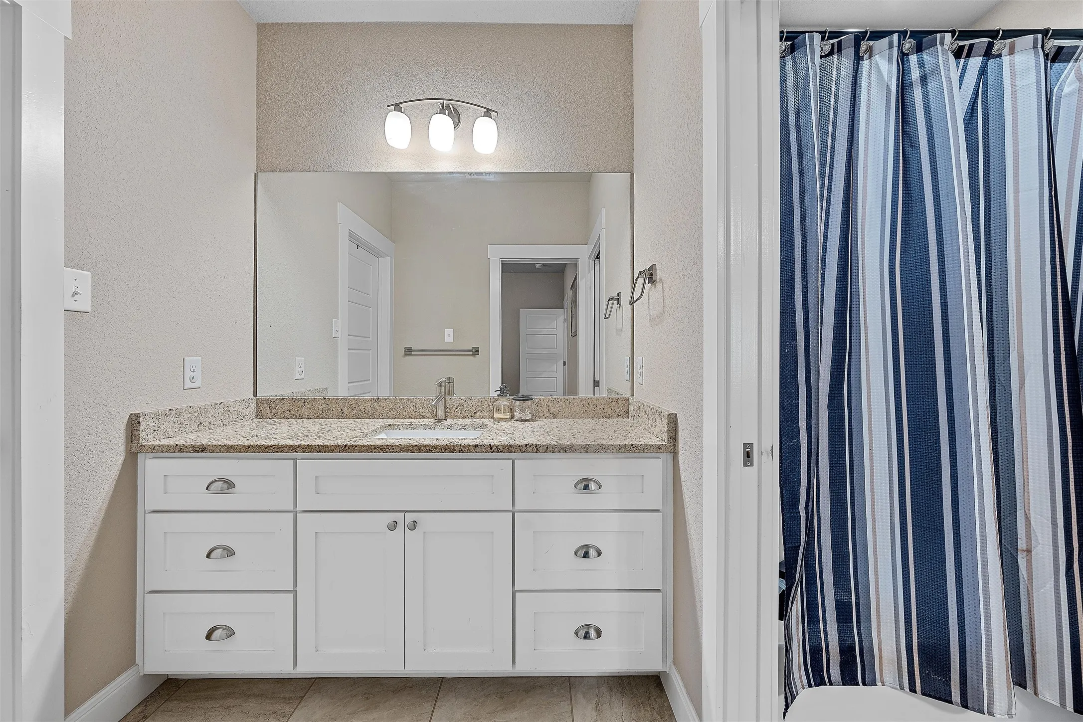 Bathroom vanity featuring a light-colored countertop, undermount sink, and white cabinetry with cup pull hardware