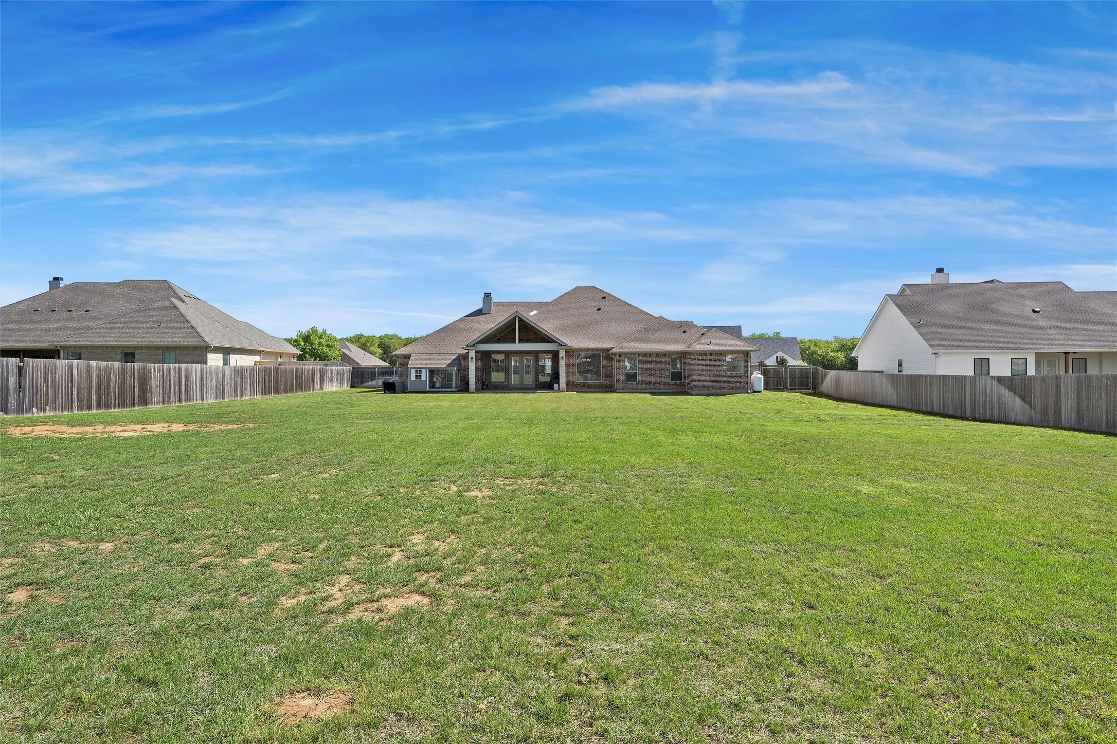 Expansive backyard featuring a large green lawn, full wood-plank fencing, and a covered patio area with a vaulted ceiling