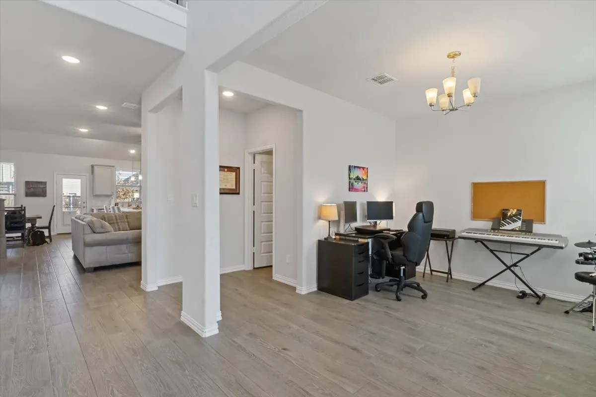 Office space featuring light wood-style floors, a chandelier, visible vents, and baseboards