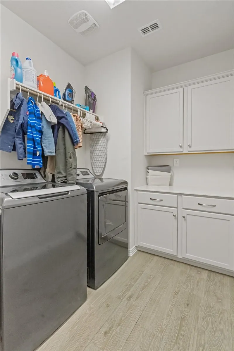 Clothes washing area with visible vents, washer and clothes dryer, cabinet space, and light wood-style floors