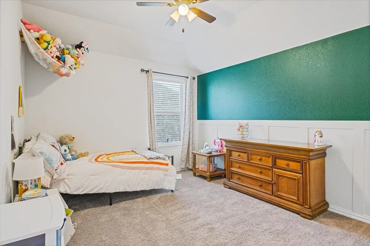 Carpeted bedroom with a wainscoted wall, ceiling fan, and vaulted ceiling
