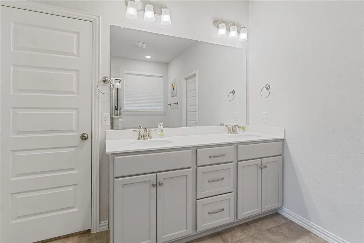 Full bath with tile patterned flooring, a sink, baseboards, and double vanity