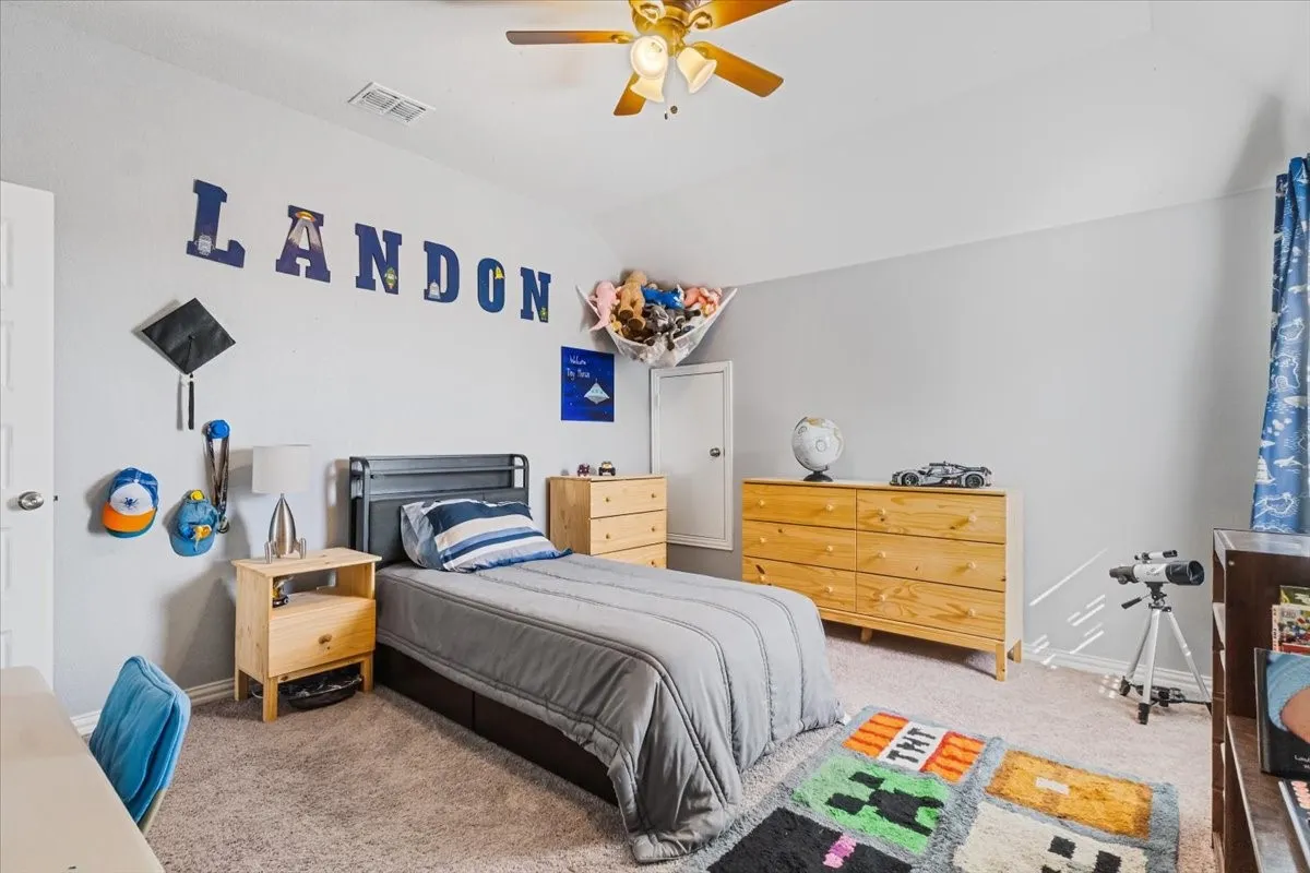 Carpeted bedroom with baseboards, visible vents, vaulted ceiling, and a ceiling fan