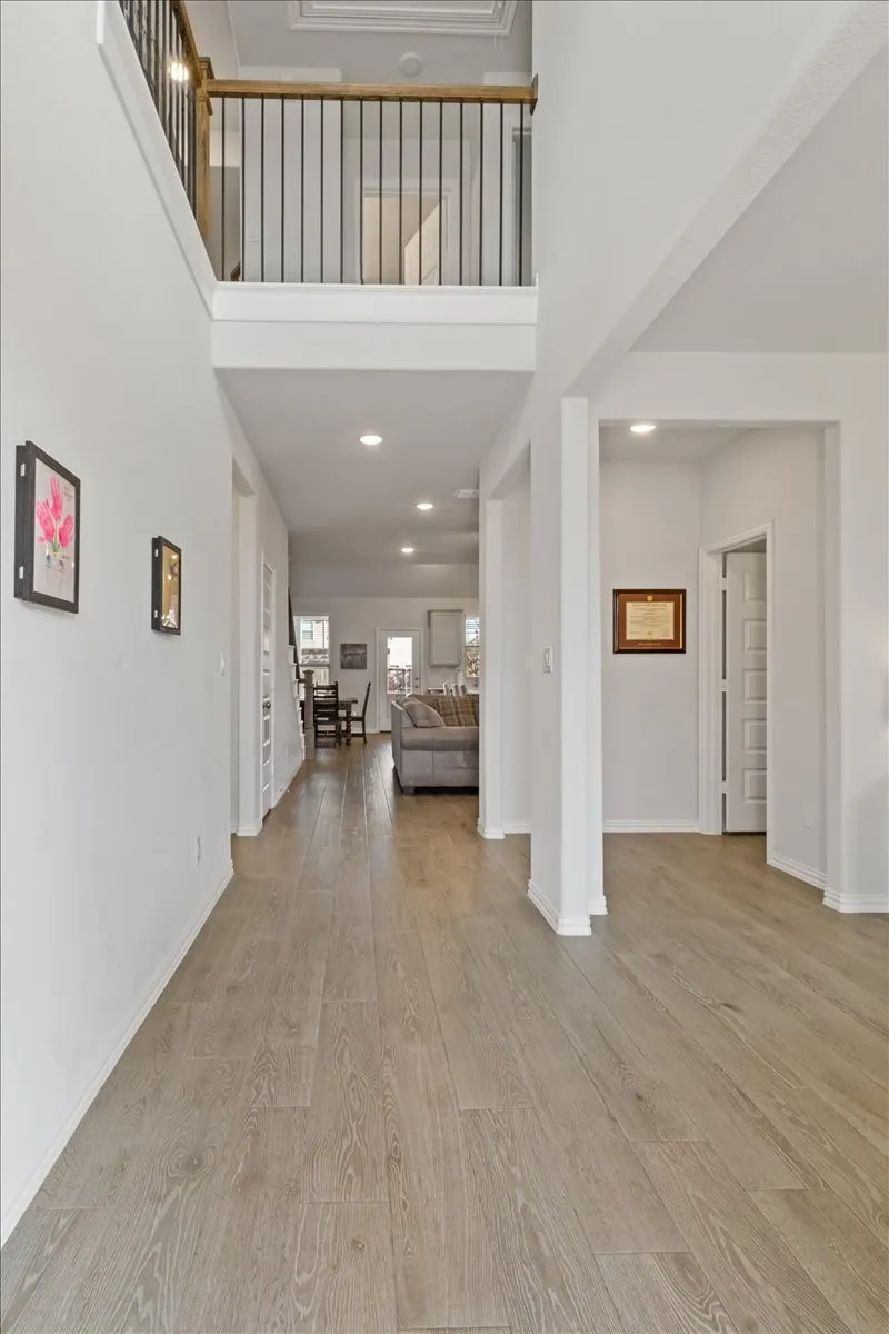 Unfurnished living room featuring baseboards, a towering ceiling, light wood-style flooring, stairs, and recessed lighting