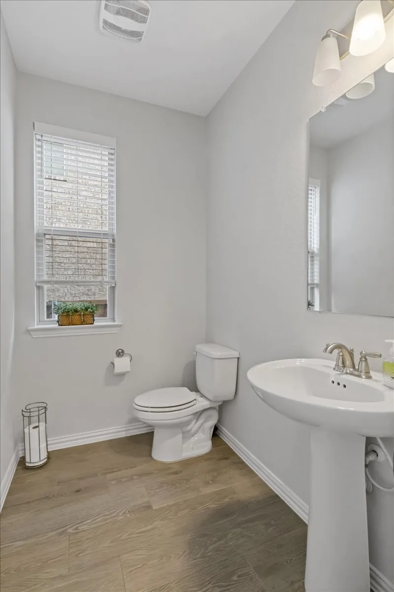 Bathroom featuring toilet, a sink, wood finished floors, visible vents, and baseboards