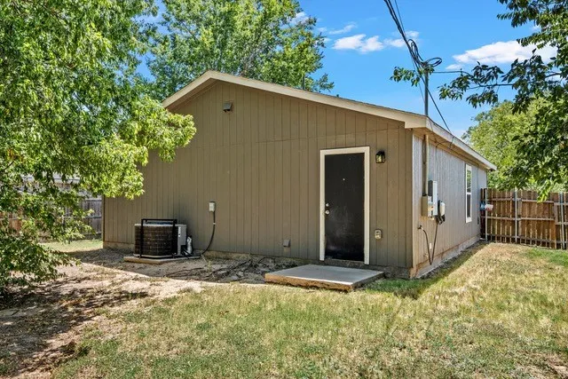 Exterior featuring vertical siding, concrete slab, black door, and a privacy fence